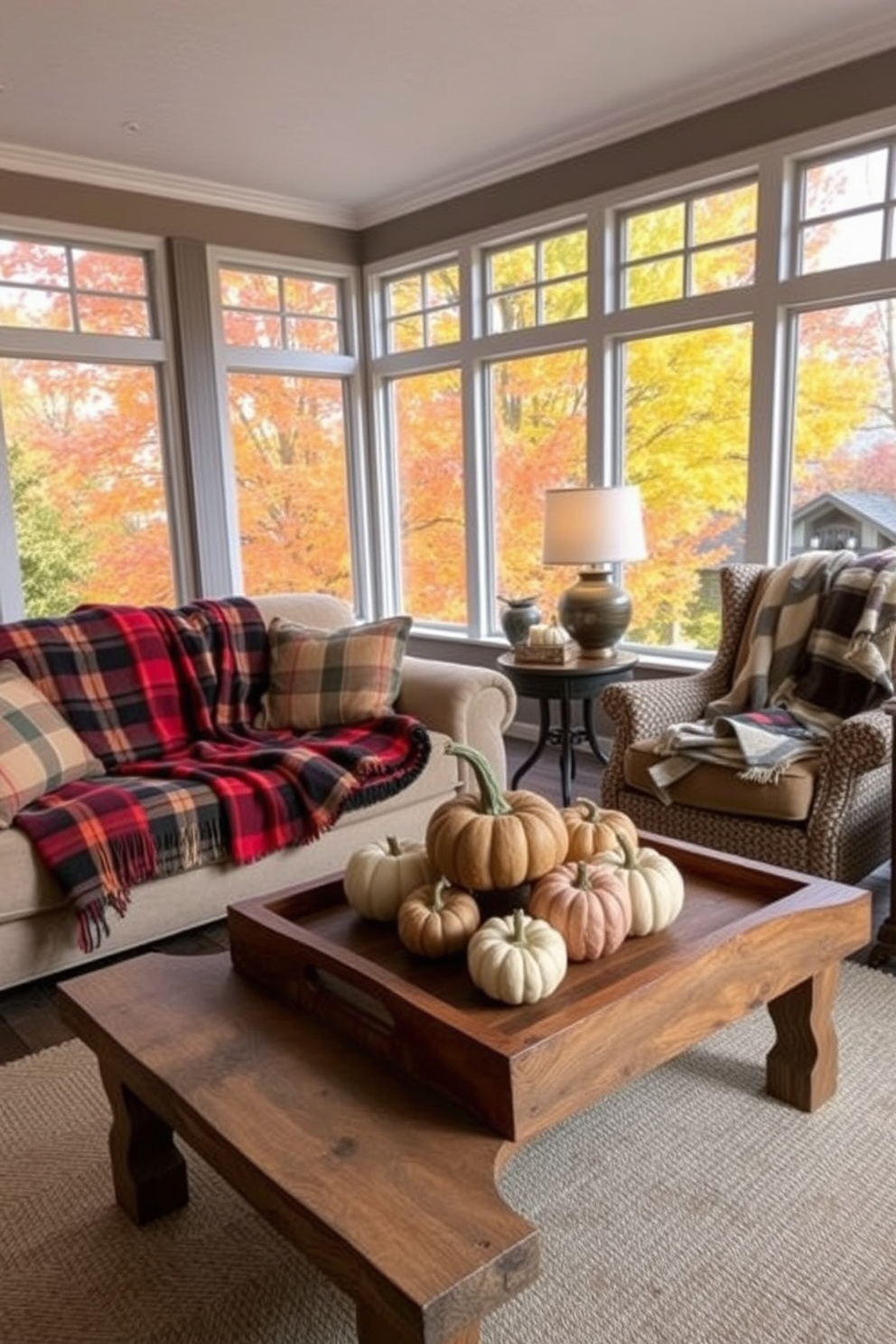 Cozy plaid throw blankets are draped over a plush sofa and an armchair, adding warmth and texture to the space. Large windows allow natural light to flood the sunroom, highlighting the vibrant autumn colors outside. Decorative pumpkins and gourds are artfully arranged on a rustic wooden coffee table, complementing the seasonal theme. Soft, ambient lighting from stylish lamps creates an inviting atmosphere perfect for relaxation.