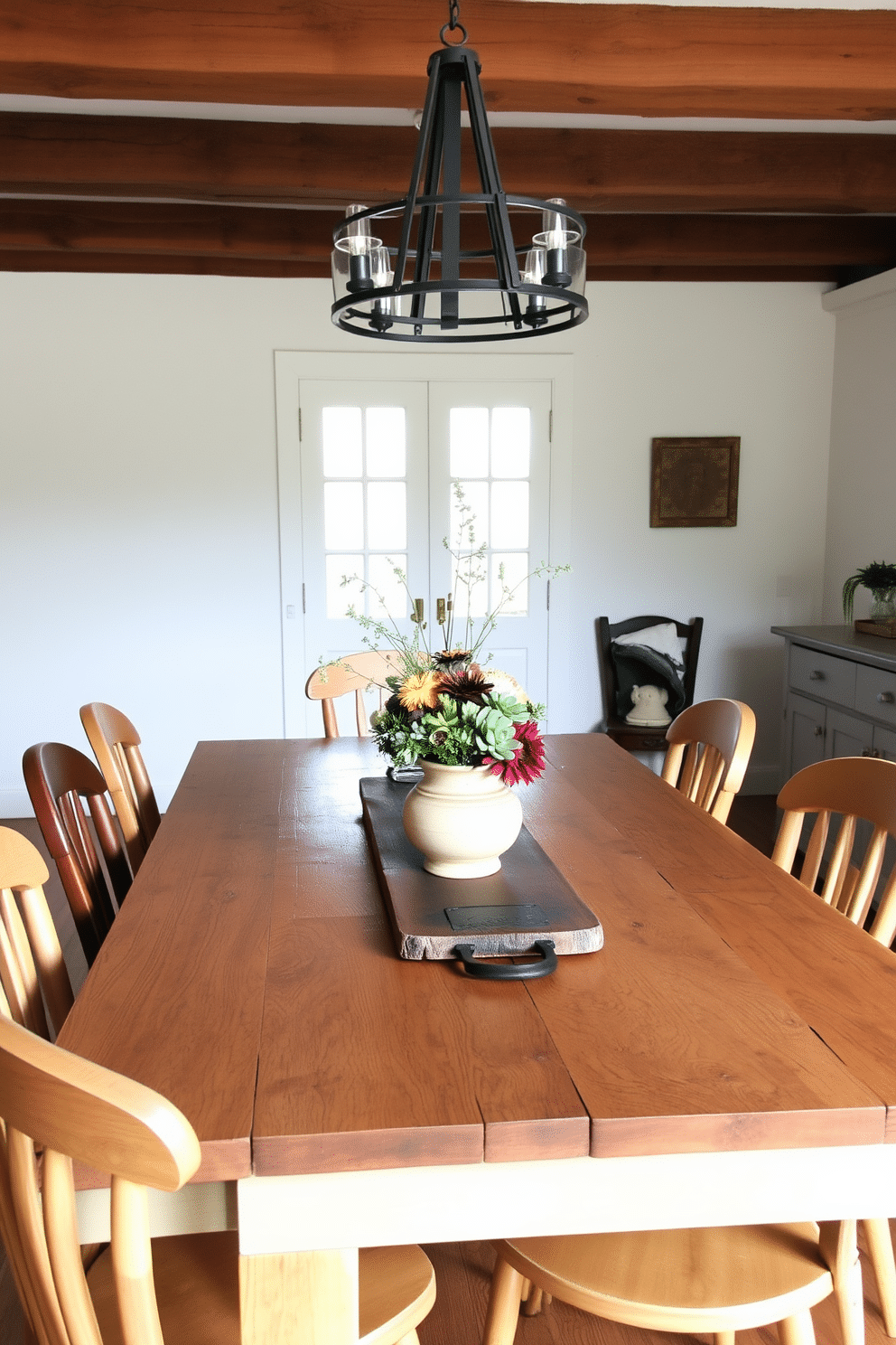 A charming farmhouse dining room features a rustic wooden table adorned with an elegant centerpiece of succulents and seasonal flowers in a vintage ceramic vase. Surrounding the table are mismatched wooden chairs, each with its own unique character, set against a backdrop of exposed beams and soft, neutral-toned walls.