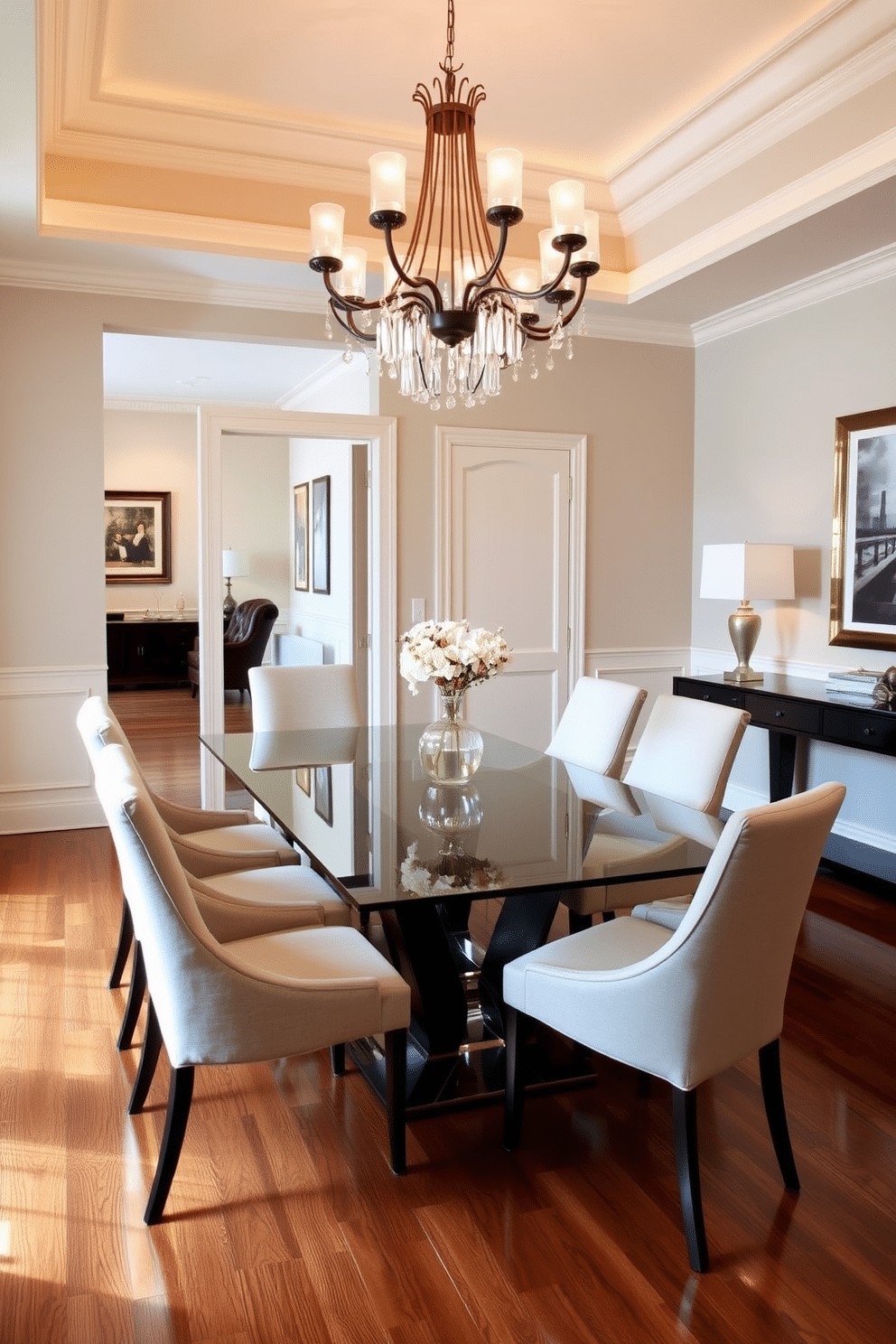 A sleek glass dining table takes center stage in a formal dining room, surrounded by elegant upholstered chairs that complement the modern aesthetic. The room is adorned with a sophisticated chandelier overhead, casting a warm glow on the polished hardwood floor and highlighting the tasteful artwork on the walls.