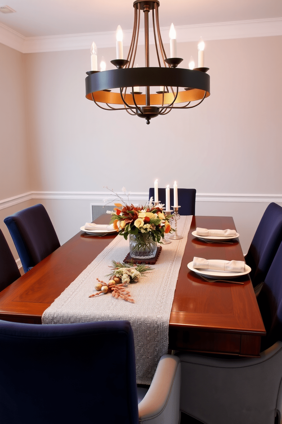 A chic table runner adorned with seasonal decor stretches elegantly across a polished wooden dining table. Surrounding the table are upholstered chairs in a rich navy fabric, complemented by a stunning chandelier that casts a warm glow over the setting. The table is styled with an assortment of decorative elements, including a centerpiece of seasonal flowers in a sleek vase. Soft, ambient lighting highlights the textures of the table runner and the intricate details of the place settings, creating an inviting atmosphere for gatherings.