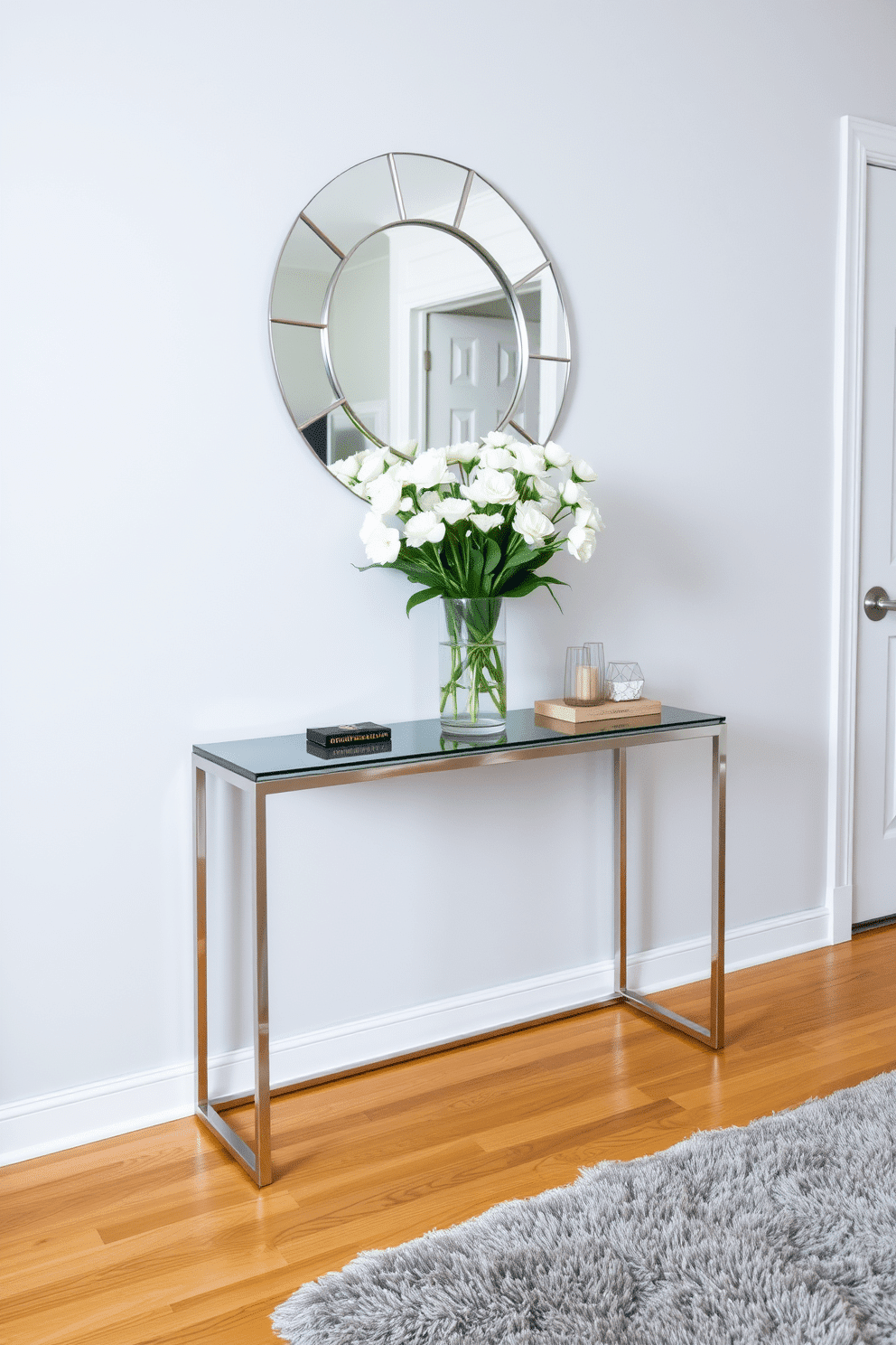 A chic console table is positioned against a soft gray wall, adorned with a decorative vase filled with fresh white flowers. The table features a sleek, modern design with clean lines, complemented by a stylish mirror hanging above it, reflecting light into the foyer. The flooring is a warm hardwood, enhancing the inviting atmosphere of the space. To the side, a plush area rug adds texture and warmth, while a few carefully placed decorative items on the table provide a personal touch.