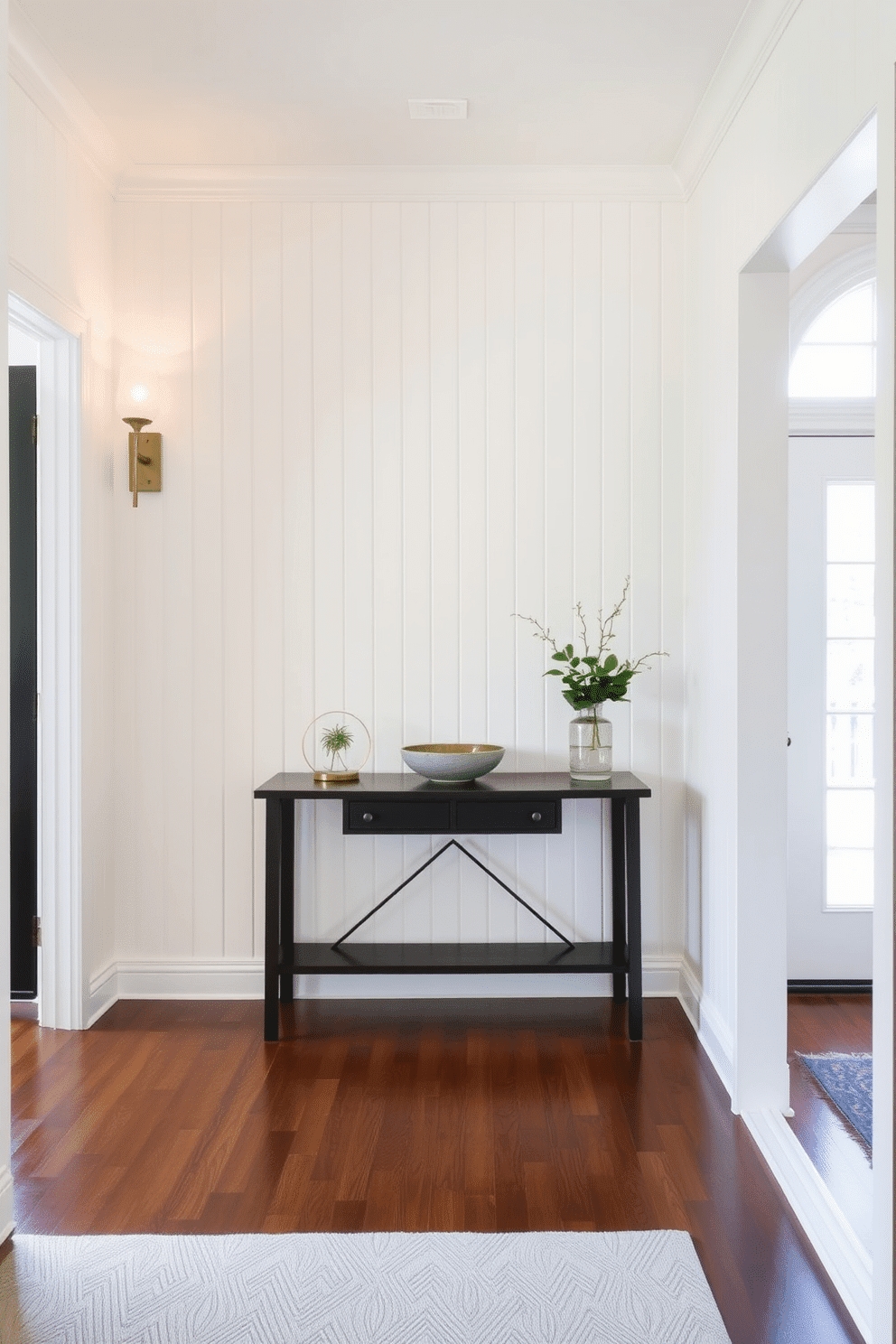 A striking foyer features an accent wall adorned with vertical shiplap, painted in a soft, creamy white that brightens the space. Flanking the wall are elegant sconces that cast a warm glow, enhancing the inviting atmosphere of the entryway. The floor is laid with rich, dark hardwood that contrasts beautifully with the light shiplap, while a stylish console table sits against the wall. On the table, a decorative bowl and a small potted plant add a touch of greenery, creating a welcoming focal point for guests.