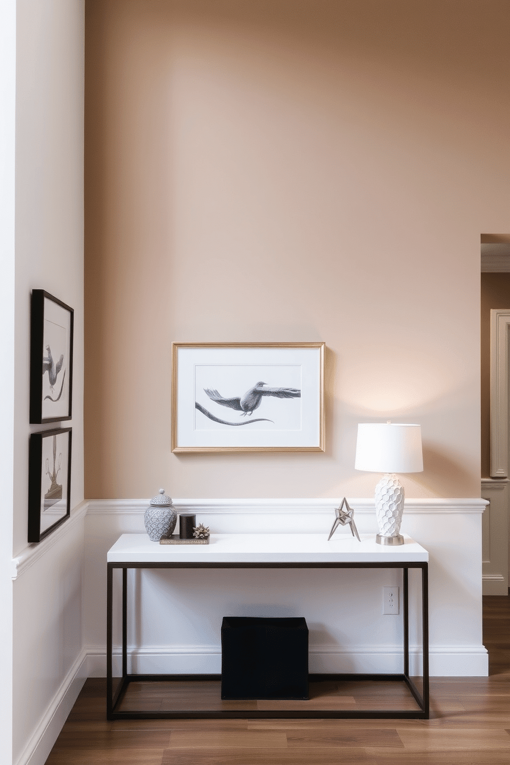 A stunning foyer wall design featuring a subtle ombre effect that transitions from soft beige at the bottom to a deep taupe at the top. The wall is adorned with elegant framed artwork that complements the color gradient, and a sleek console table sits below, topped with decorative accents and a stylish lamp.