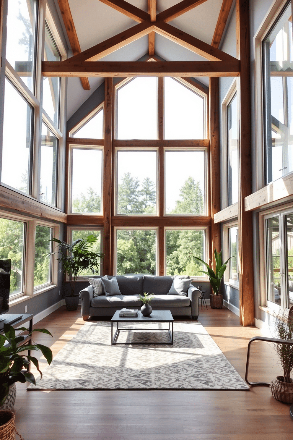 A spacious attic room with large windows allowing abundant natural light to flood the space. The walls are painted in a soft gray, complemented by exposed wooden beams that add character and warmth. The room features a cozy seating area with a plush gray sofa and a stylish coffee table, creating an inviting atmosphere. A large area rug anchors the space, while decorative plants in the corners enhance the room's fresh and airy feel.