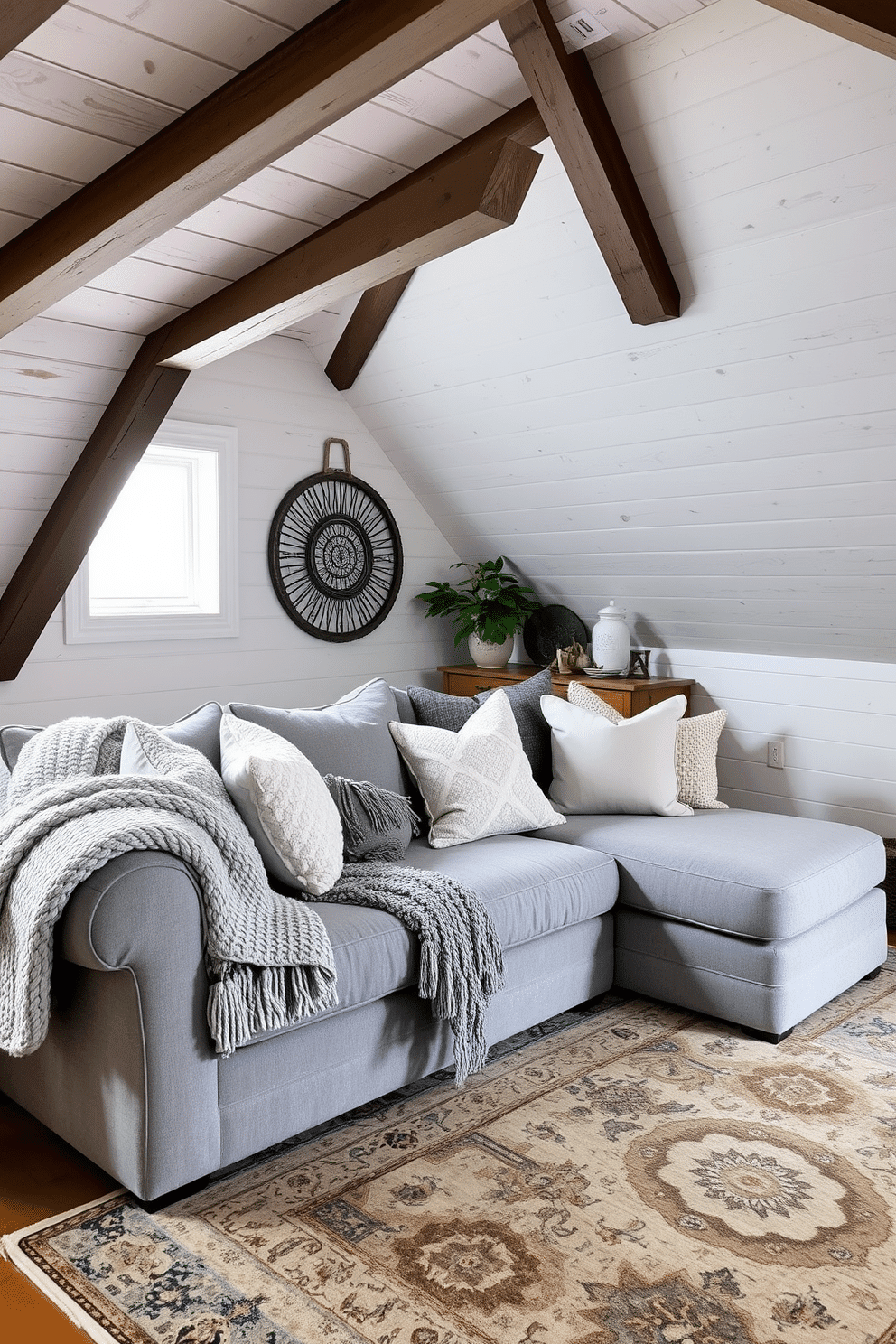 A cozy gray attic room featuring a mix of textures for a layered look. The walls are clad in soft gray shiplap, while the ceiling showcases exposed wooden beams, creating a warm and inviting atmosphere. A plush, oversized gray sectional sofa is adorned with a variety of textured throw pillows in different shades of gray and silver. A chunky knit throw is draped over the armrest, and a vintage area rug with intricate patterns adds depth to the space.