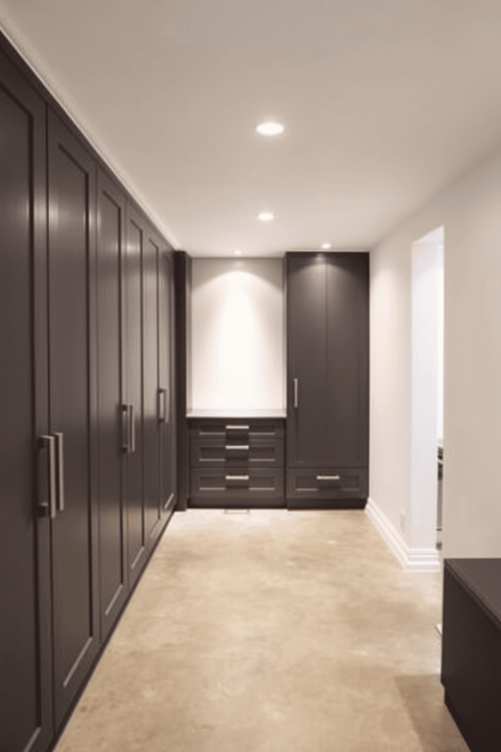 A modern basement featuring built-in cabinetry in charcoal gray, seamlessly integrated into the design for a sleek and sophisticated look. The cabinetry includes ample storage space with minimalist handles, complementing the overall aesthetic of the room. The walls are painted in a soft white to enhance the brightness of the space, while the flooring consists of polished concrete for a contemporary feel. Accent lighting highlights the cabinetry, creating an inviting atmosphere perfect for relaxation or entertainment.