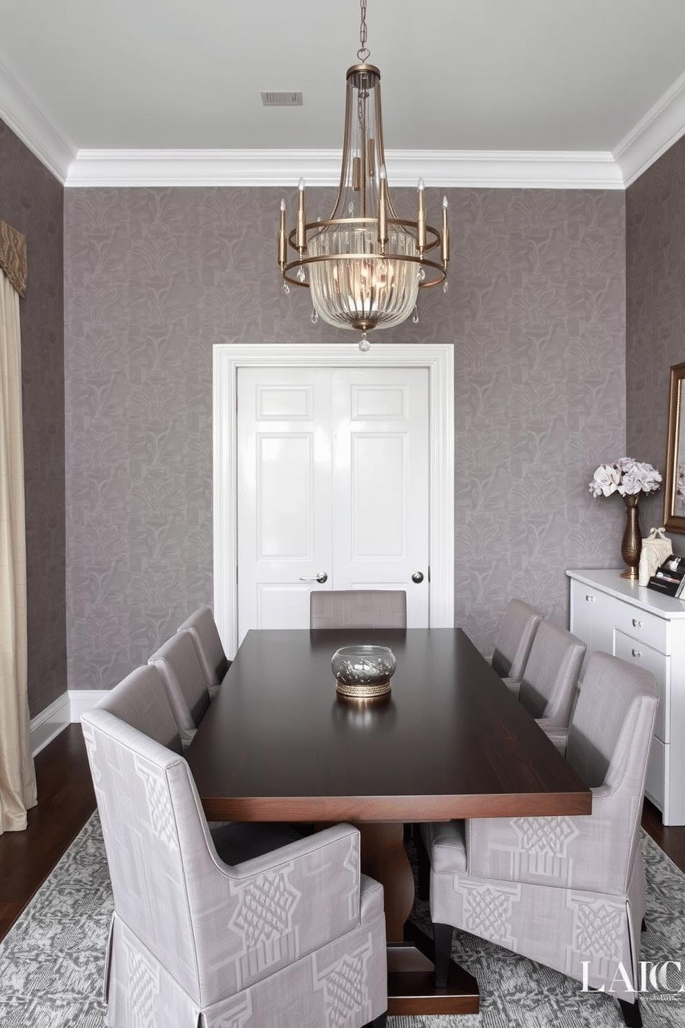 Chic gray wallpaper with geometric patterns adorns the walls of a modern dining room, creating a stylish backdrop for the space. A sleek, rectangular dining table in a dark wood finish is surrounded by upholstered chairs in a complementary gray fabric, enhancing the room's contemporary aesthetic. A stunning chandelier with metallic accents hangs above the table, casting a warm glow over the dining area. To one side, a minimalist sideboard in white provides additional storage and display space for decorative items, contributing to the room's elegant ambiance.