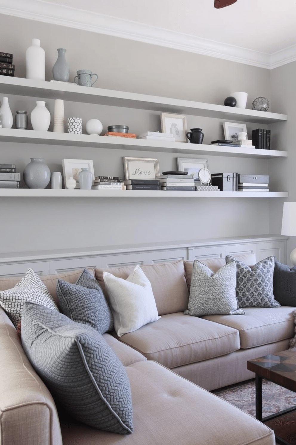 A cozy family room featuring open shelving that displays an array of gray decor items, including vases, books, and decorative boxes. The walls are painted a soft gray, complementing a plush sectional sofa adorned with textured throw pillows in varying shades of gray.