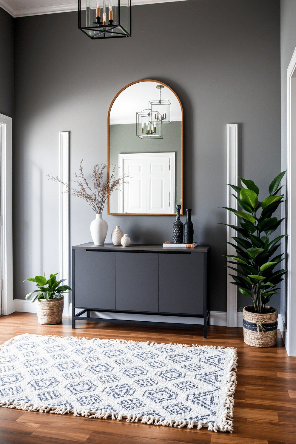 A stylish foyer featuring gray walls complemented by white trim accents creates a modern and inviting atmosphere. The space includes a sleek console table with a minimalist design, adorned with decorative objects and a large mirror above for added depth. A plush area rug in a geometric pattern lies beneath, adding warmth and texture to the entryway. Flanking the foyer are potted plants that bring a touch of nature indoors, enhancing the overall aesthetic with a pop of greenery.