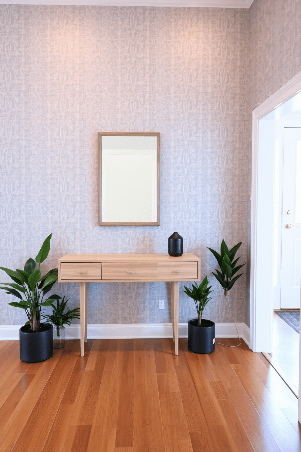 A stylish foyer with gray wallpaper featuring subtle, elegant patterns that add depth without overwhelming the space. The flooring is a sleek, polished hardwood that complements the soft tones of the wallpaper, creating a warm and inviting atmosphere. To the left, a modern console table in a light wood finish holds a decorative mirror with a minimalist frame. Flanking the table are two potted plants that introduce a touch of greenery, enhancing the overall aesthetic of the foyer.