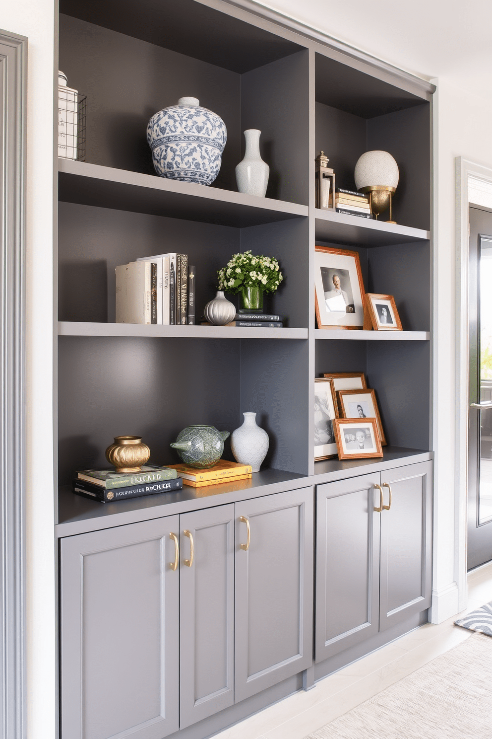 A stylish foyer featuring open shelving in a sleek gray finish, showcasing an array of decorative items such as books, vases, and framed photos. The walls are painted in a soft white hue, complementing the gray shelving and creating a bright, welcoming atmosphere.