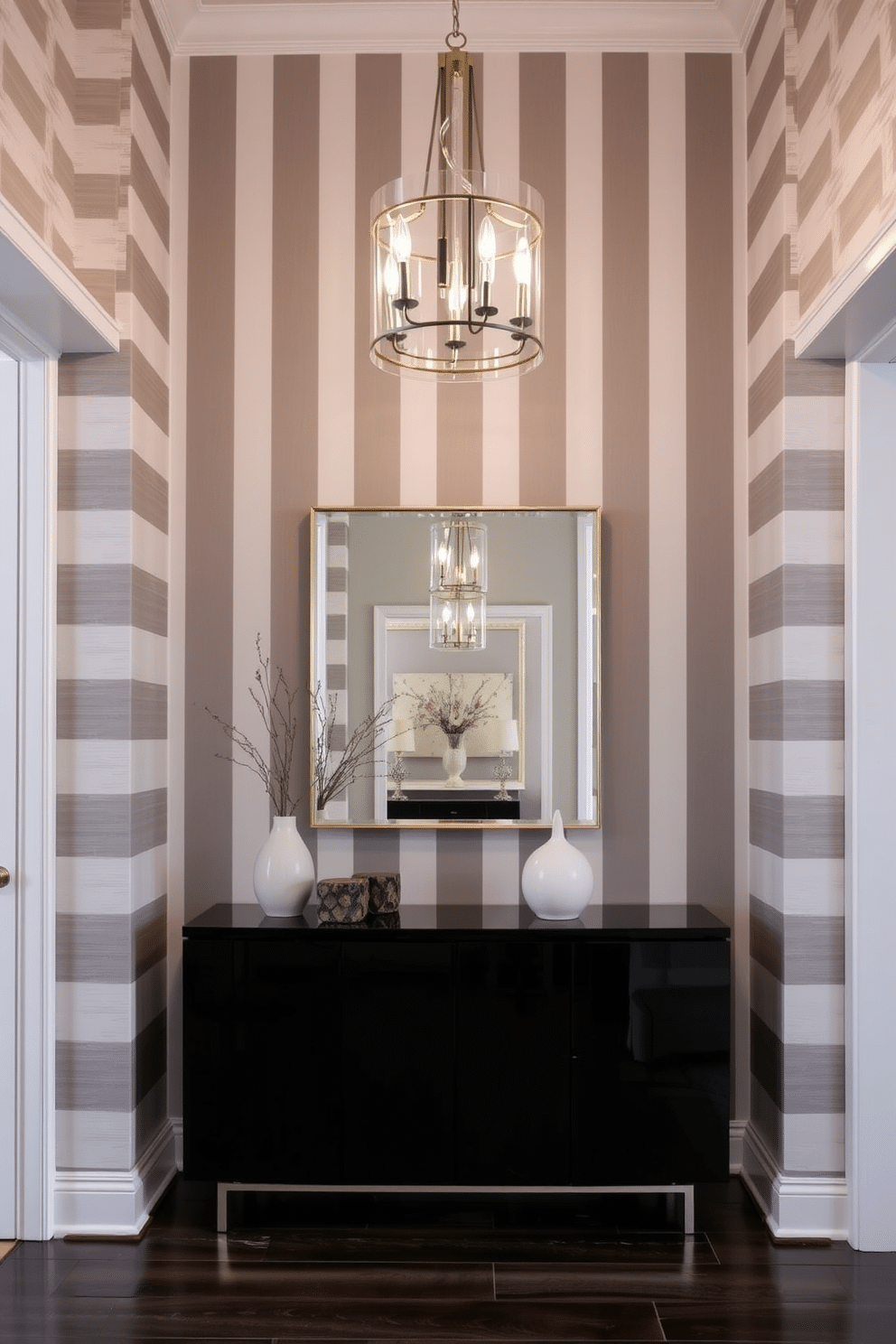 A stunning foyer features gray and white striped wallpaper that adds a touch of elegance and sophistication. The space is illuminated by a modern chandelier, casting a warm glow over a sleek console table adorned with decorative objects and a stylish mirror above it.