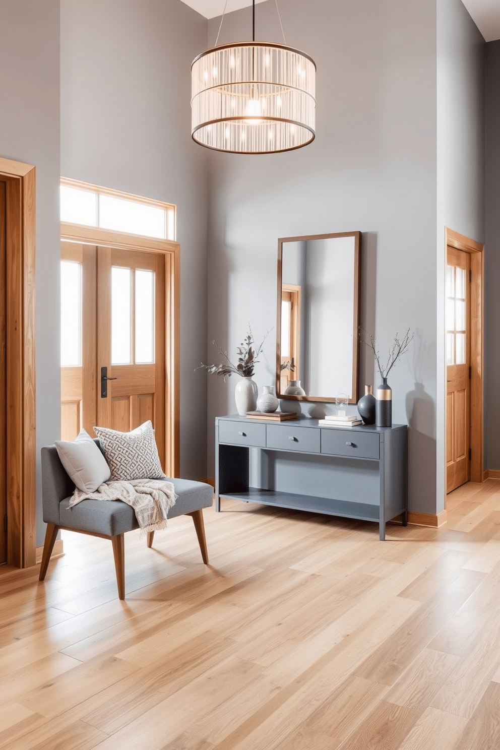 A stylish foyer featuring a harmonious blend of gray walls and natural wood accents. The floor is adorned with wide plank natural wood, while a sleek gray console table stands against the wall, topped with decorative items and a large mirror. To the left, a cozy seating area includes a gray upholstered bench with wooden legs, complemented by a soft, textured throw. A statement light fixture hangs above, casting a warm glow over the space, enhancing the inviting atmosphere.