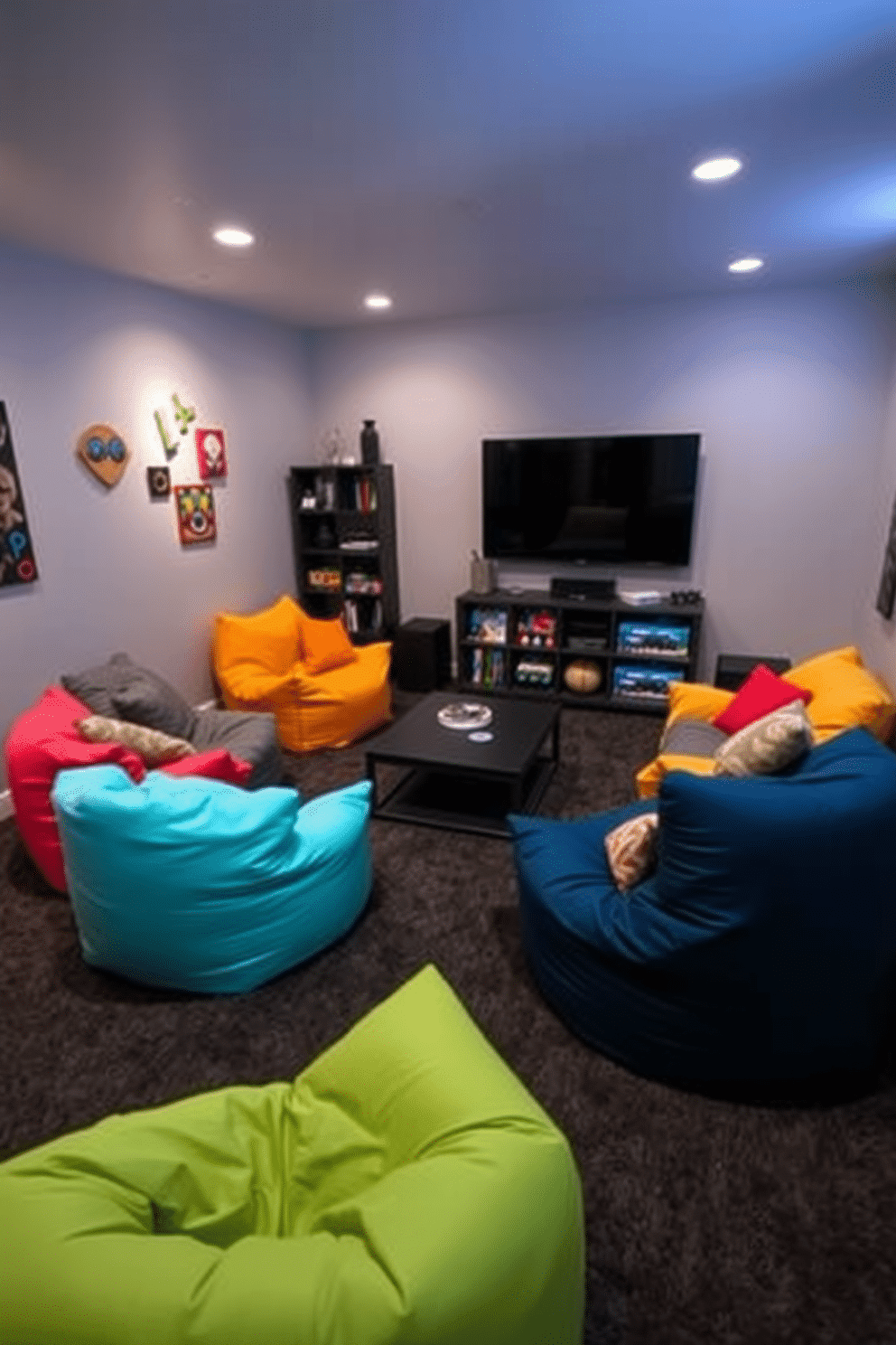 A cozy game room featuring several colorful bean bags arranged in a semi-circle around a low coffee table. The walls are painted a soft gray, complemented by playful wall art and ambient lighting that creates a relaxed atmosphere. In one corner, a large flat-screen TV is mounted on the wall, surrounded by shelves filled with games and entertainment accessories. The flooring is a plush, dark carpet that adds warmth to the space, making it inviting for casual gatherings.