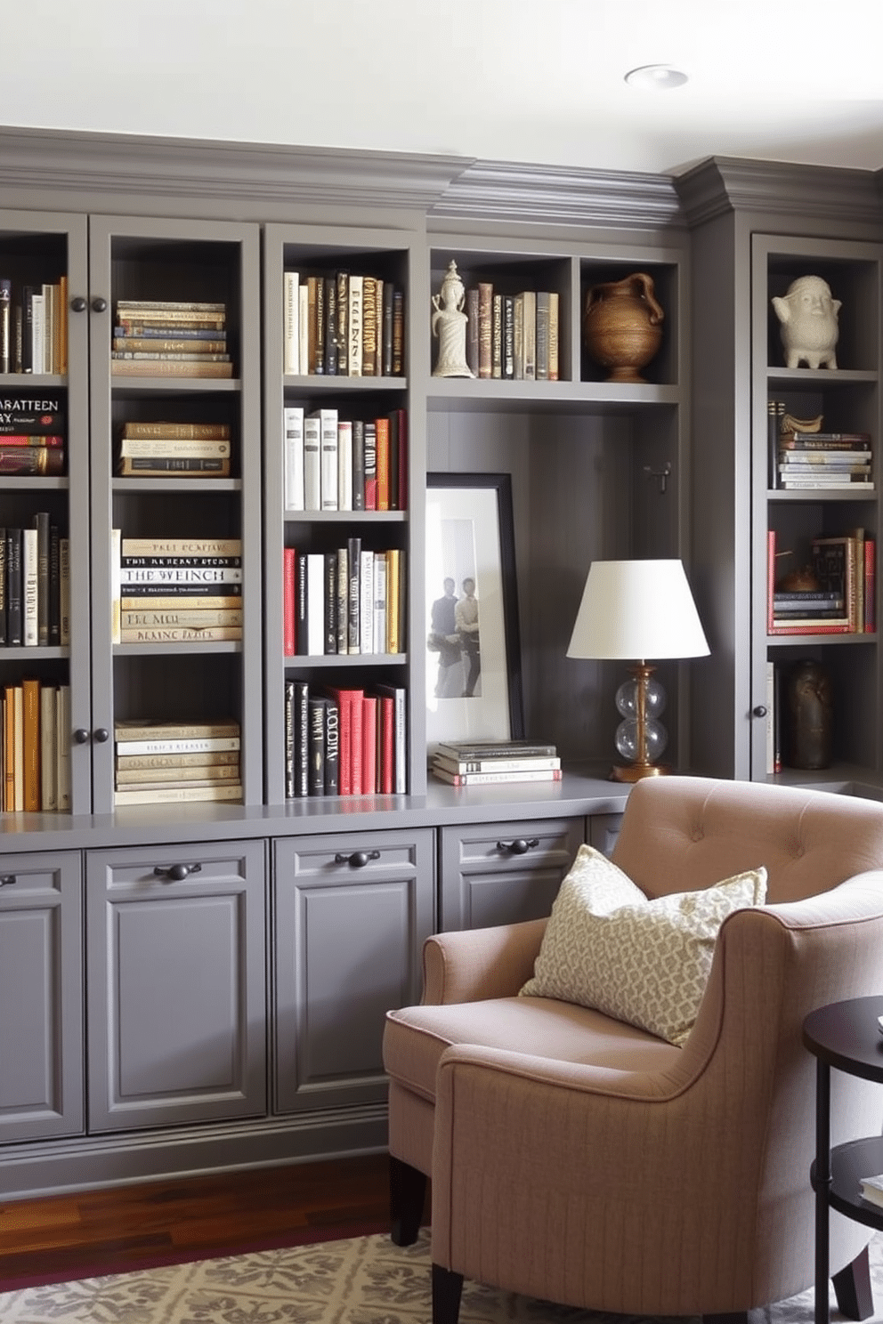 A cozy gray home library featuring built-in cabinetry that provides organized storage for books and decorative items. The cabinetry is complemented by a plush reading nook with a comfortable armchair and a small side table, creating an inviting atmosphere for relaxation and study.