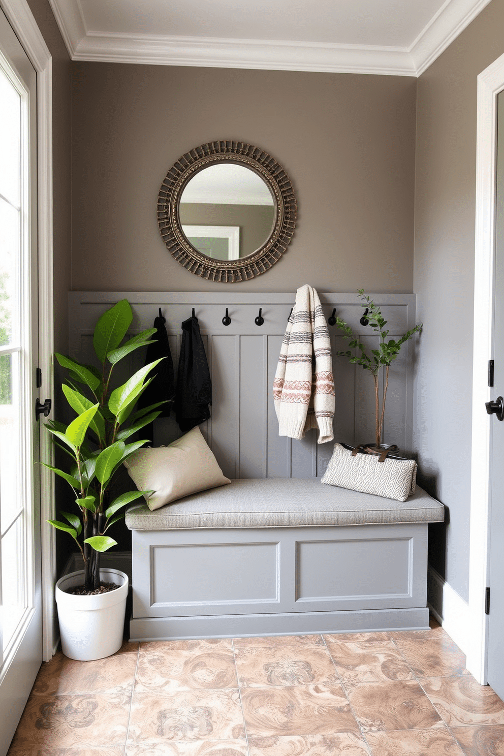 A cozy gray bench with storage underneath sits against the wall in a stylish mudroom, providing both functionality and comfort. The bench is upholstered in soft fabric, and above it, a row of hooks holds jackets and bags, while a decorative mirror reflects the natural light coming through the nearby window. The mudroom features a warm color palette with gray walls and a durable, patterned tile floor that adds visual interest. Potted plants in the corners bring a touch of nature indoors, creating an inviting atmosphere perfect for welcoming guests.