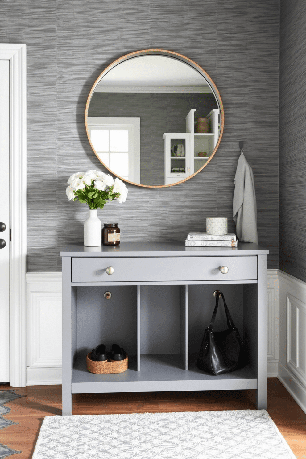 A stylish gray console table serves as a functional accent piece in the mudroom, featuring clean lines and a sleek finish. Above the table, a large round mirror with a minimalist frame reflects natural light, enhancing the spacious feel of the area. The mudroom is designed with practical storage solutions, including built-in cubbies and hooks for coats and bags. A textured gray wallpaper adds depth to the space, while a durable, patterned rug defines the entryway and complements the console table.