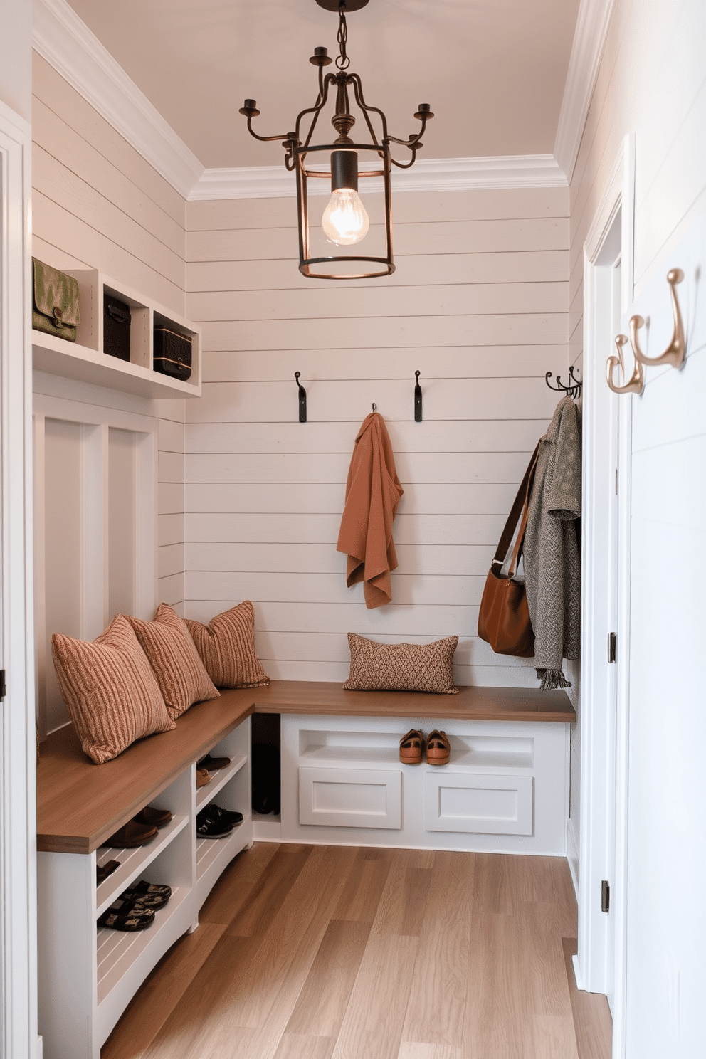 Light gray shiplap walls create a textured backdrop, enhancing the cozy atmosphere of the mudroom. The space features built-in benches with plush cushions, alongside open shelving for easy access to shoes and accessories. A statement light fixture hangs from the ceiling, casting a warm glow over the room. Decorative hooks line the walls, providing a stylish solution for hanging coats and bags.