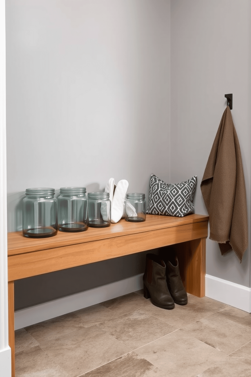 A modern mudroom featuring gray glass jars for small item storage, neatly arranged on a sleek wooden shelf. The walls are painted in a soft gray hue, complemented by a durable, textured tile floor that enhances the space's functionality.