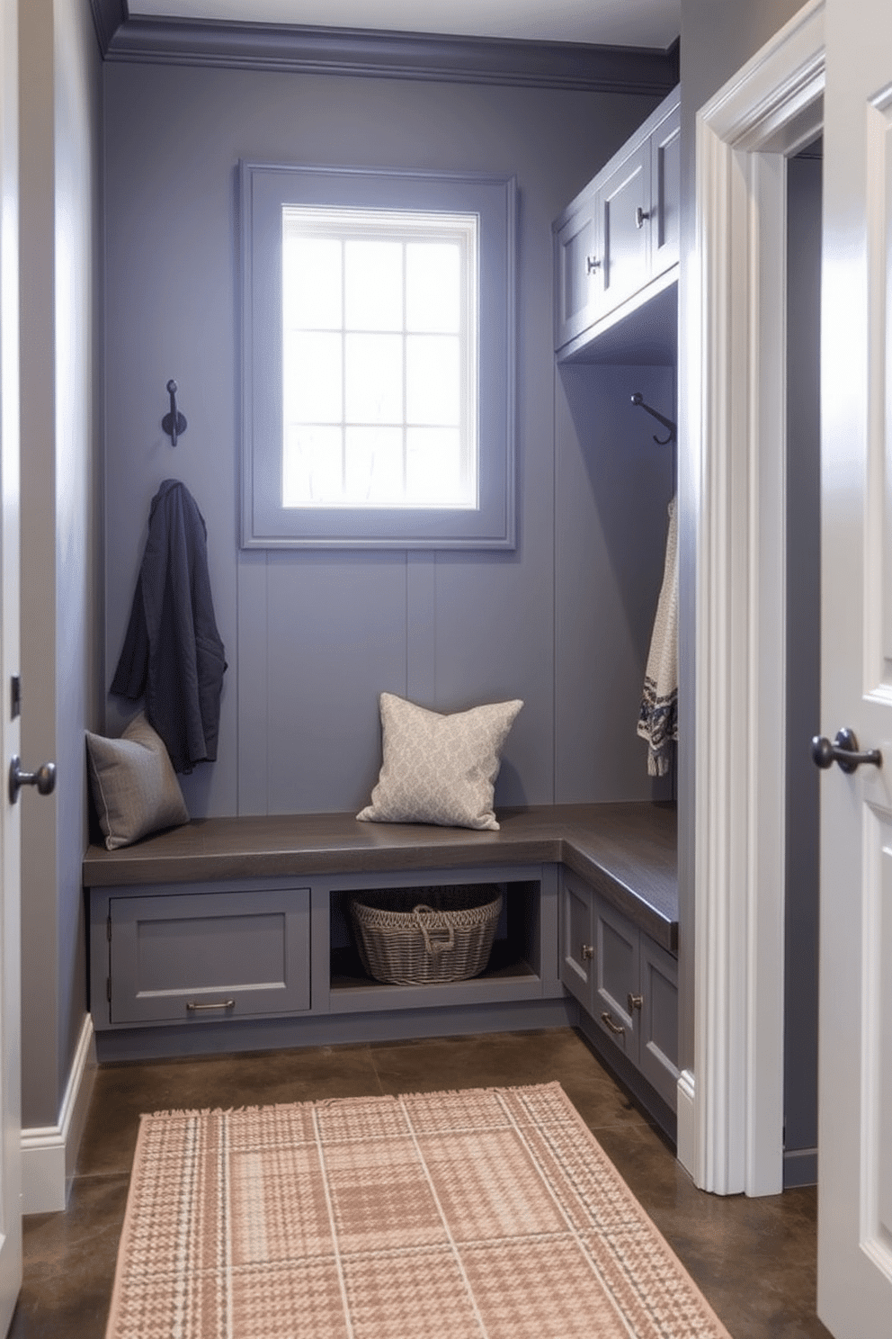 A contemporary gray mudroom features a stylish gray framed mirror that reflects the natural light flooding in from a nearby window. The space is equipped with built-in storage benches and hooks for coats, while a textured rug adds warmth to the polished concrete floor.