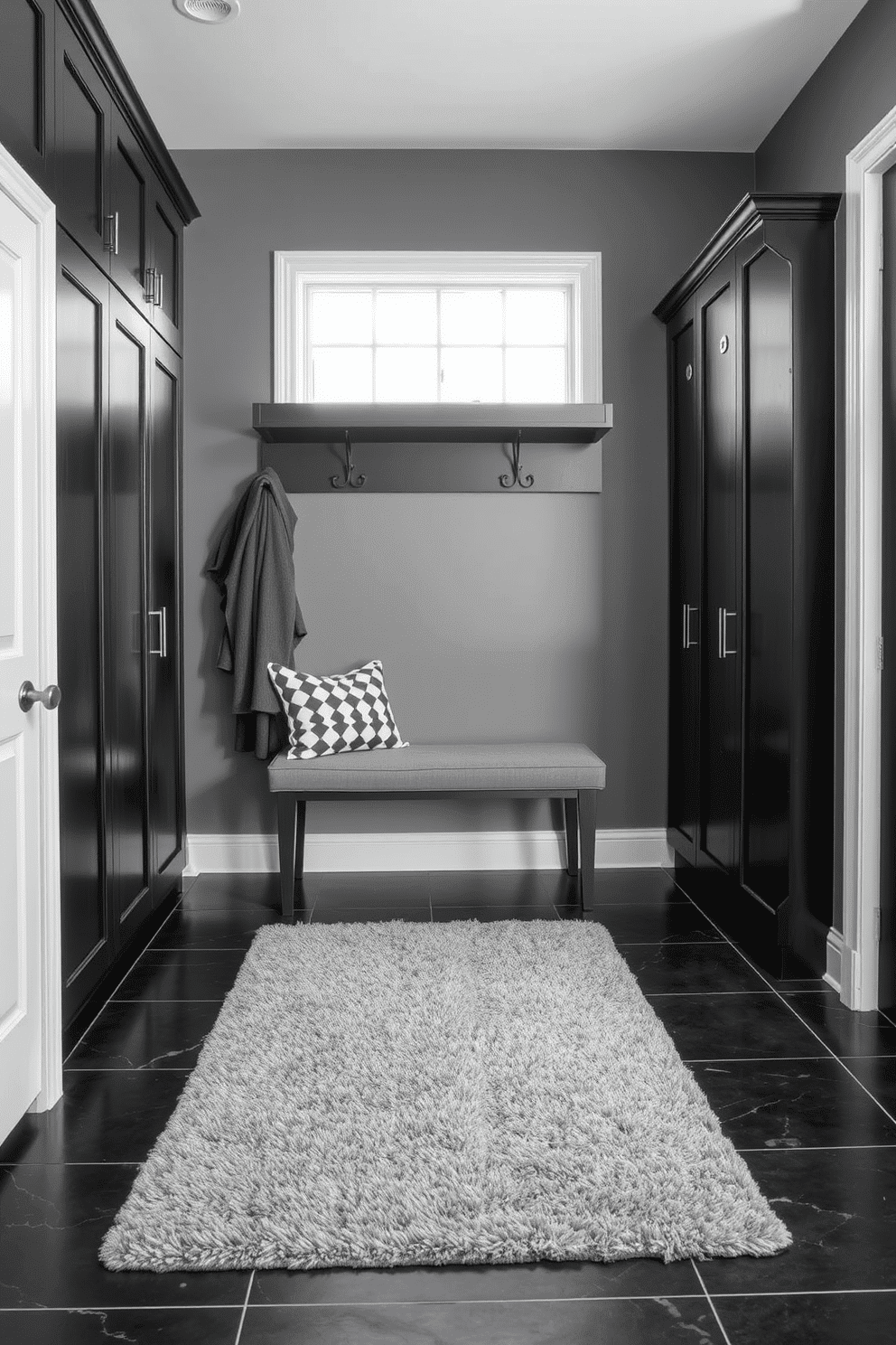 A sophisticated mudroom featuring a gray and black color scheme. The walls are painted in a deep charcoal gray, complemented by sleek black cabinetry and a stylish bench with gray upholstery. The floor is adorned with large black tiles that contrast beautifully with a plush gray area rug. Decorative hooks for coats and a minimalist shelf for storage enhance the functionality while maintaining an elegant aesthetic.