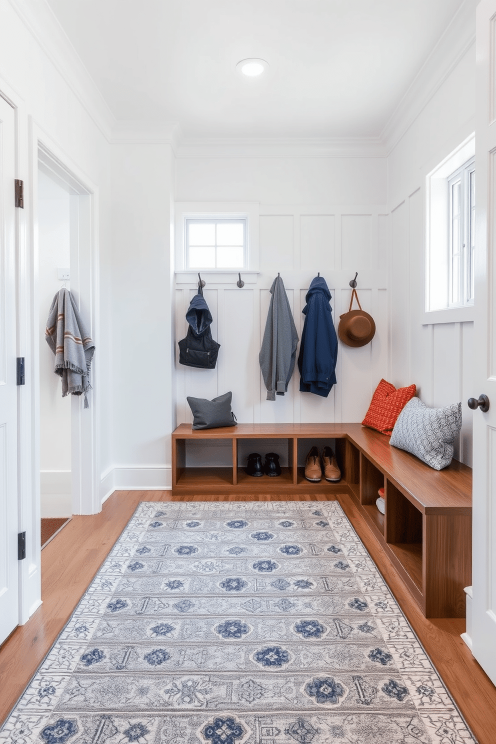 A stylish mudroom featuring a gray area rug that defines the space, providing warmth and texture underfoot. The walls are painted in a soft white, complemented by built-in wooden storage benches and hooks for coats, creating an organized and inviting entryway.