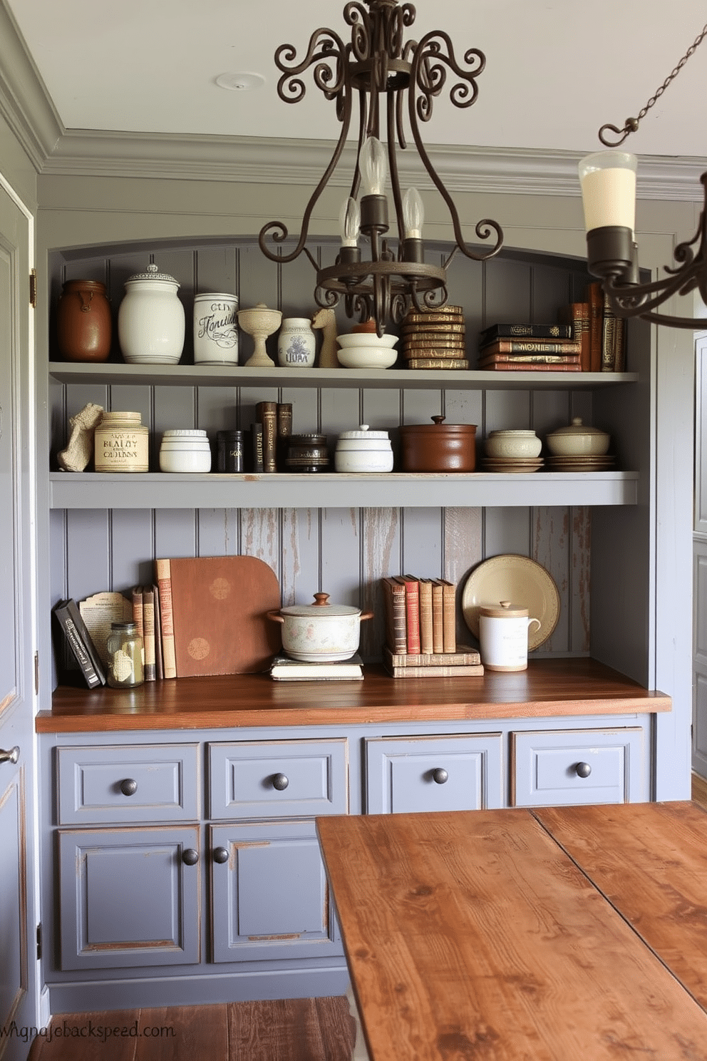 A distressed gray pantry features vintage accents, with open shelving showcasing rustic ceramic jars and antique cookbooks. The walls are adorned with reclaimed wood paneling, and an ornate, wrought-iron light fixture hangs above a weathered farmhouse table.