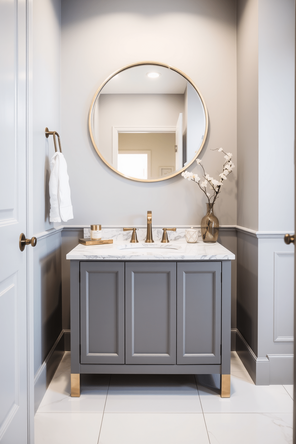 A sleek gray vanity with gold accents takes center stage in a modern powder room. The walls are painted in a soft gray hue, complementing the elegant design of the vanity. Above the vanity, a stylish round mirror with a gold frame reflects the ambient light. The floor is adorned with large white tiles, adding a touch of luxury to the space.