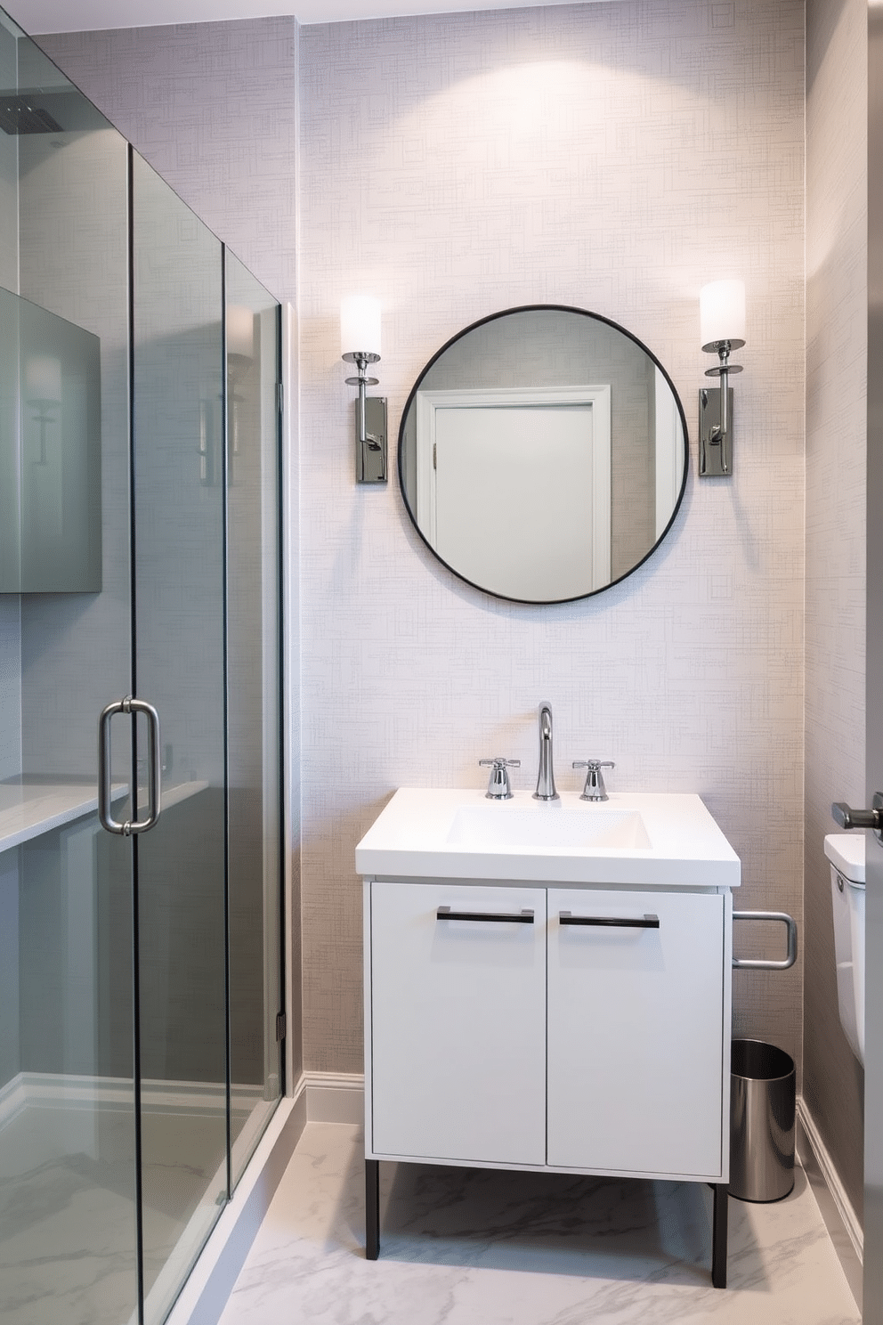 A chic powder room featuring a gray glass shower enclosure that exudes elegance. The walls are adorned with subtle gray wallpaper, complemented by a sleek white vanity with a polished chrome faucet. A large round mirror with a thin black frame hangs above the vanity, reflecting the soft ambient lighting from stylish sconces. The floor is covered in a luxurious gray and white marble tile, enhancing the overall sophisticated atmosphere.