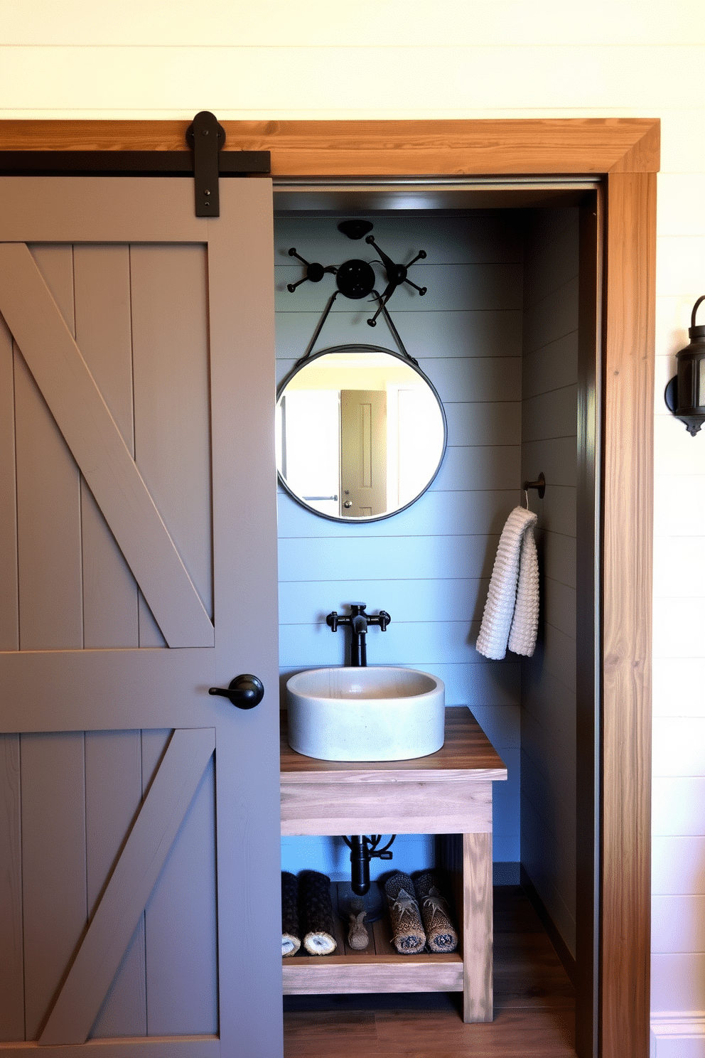 A rustic gray barn door swings open to reveal a cozy powder room, featuring a reclaimed wood vanity with a natural stone sink. The walls are adorned with shiplap in a soft gray hue, complemented by vintage-inspired fixtures and a round mirror with a wrought iron frame.