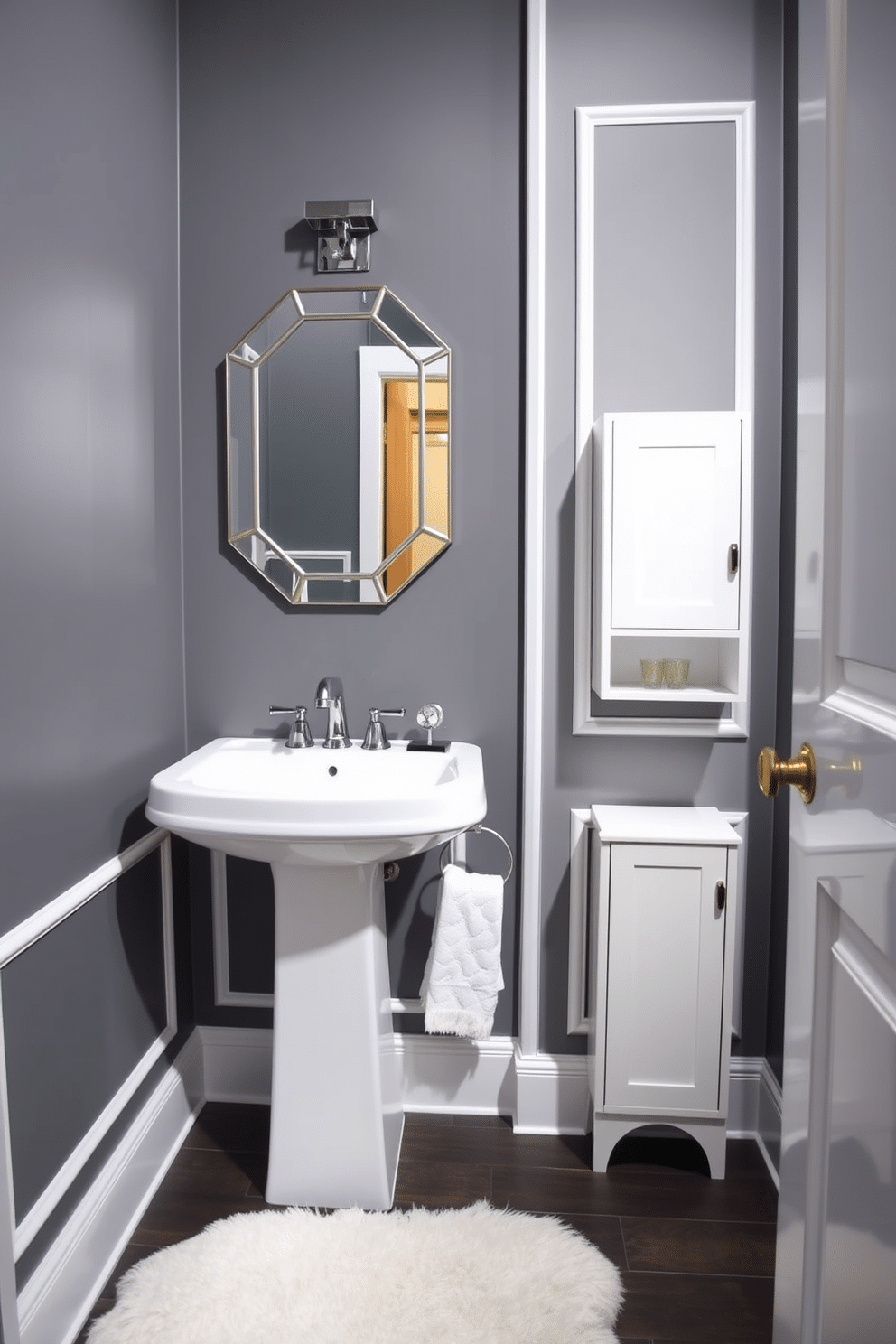 A chic powder room featuring bold gray walls accented with crisp white trim. The space includes a sleek pedestal sink with a modern chrome faucet, complemented by a stylish wall-mounted mirror with a geometric frame. To the right, a compact storage cabinet with a minimalist design provides functional elegance. A plush white rug lies beneath the sink, adding warmth and comfort to the sophisticated atmosphere.