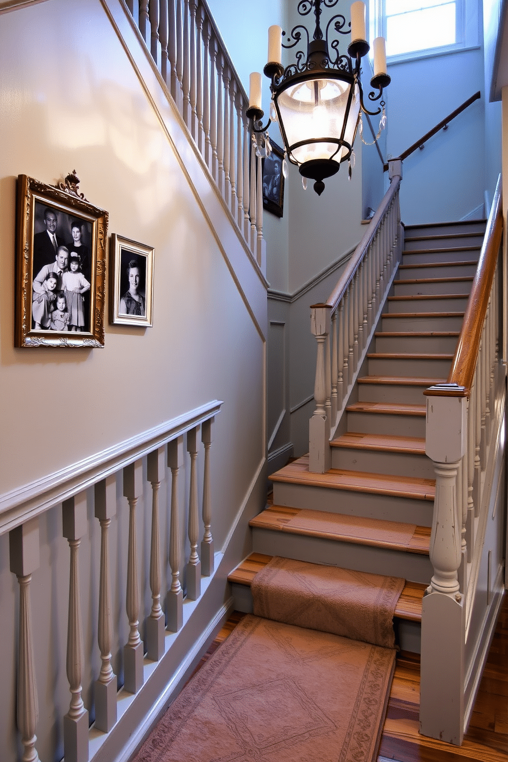 A vintage gray painted staircase features elegant spindles that add a classic touch to the design. The staircase is illuminated by a vintage chandelier, casting a warm glow on the distressed wood steps. The walls beside the staircase are adorned with black-and-white family photographs in ornate frames, enhancing the nostalgic feel. A plush runner in muted tones runs down the center of the staircase, providing comfort and style underfoot.