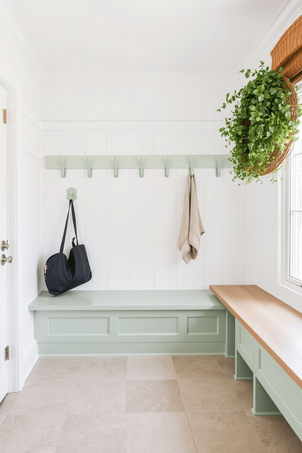 A spacious mudroom features pale green hooks mounted against a crisp white wall, creating a fresh and inviting atmosphere. The floor is adorned with large, textured tiles in a neutral tone, providing both style and durability for everyday use.