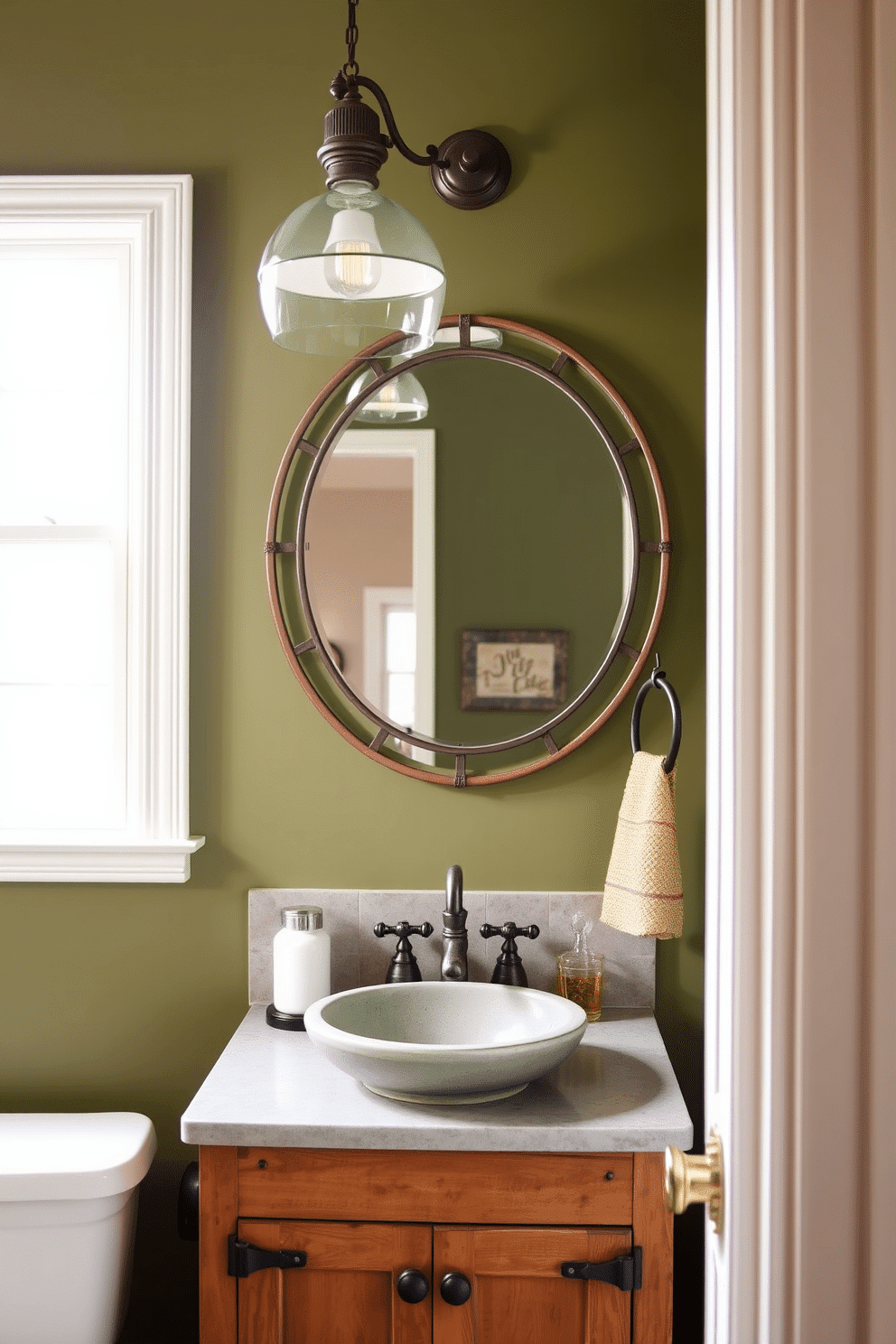 A chic powder room featuring olive green walls complemented by rustic metal finishes. The space includes a vintage-style sink with a distressed metal faucet and a wooden cabinet with iron hardware. A large round mirror with a rustic metal frame hangs above the sink, reflecting the warm ambiance. Soft, ambient lighting from a pendant fixture enhances the cozy atmosphere, while a woven basket adds a touch of texture and practicality.