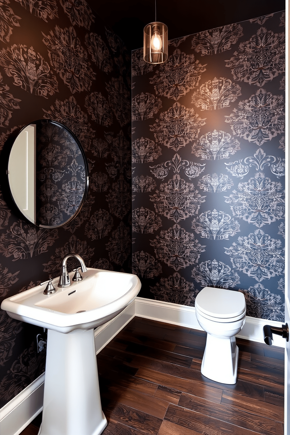 A half bath featuring bold wallpaper adorned with intricate patterns that create a striking visual impact. The space includes a sleek pedestal sink with a polished chrome faucet, complemented by a stylish round mirror framed in black. The floor is covered in dark wood planks that add warmth to the room, contrasting beautifully with the vibrant wallpaper. A small, elegant light fixture hangs from the ceiling, casting a soft glow over the space and highlighting the design details.