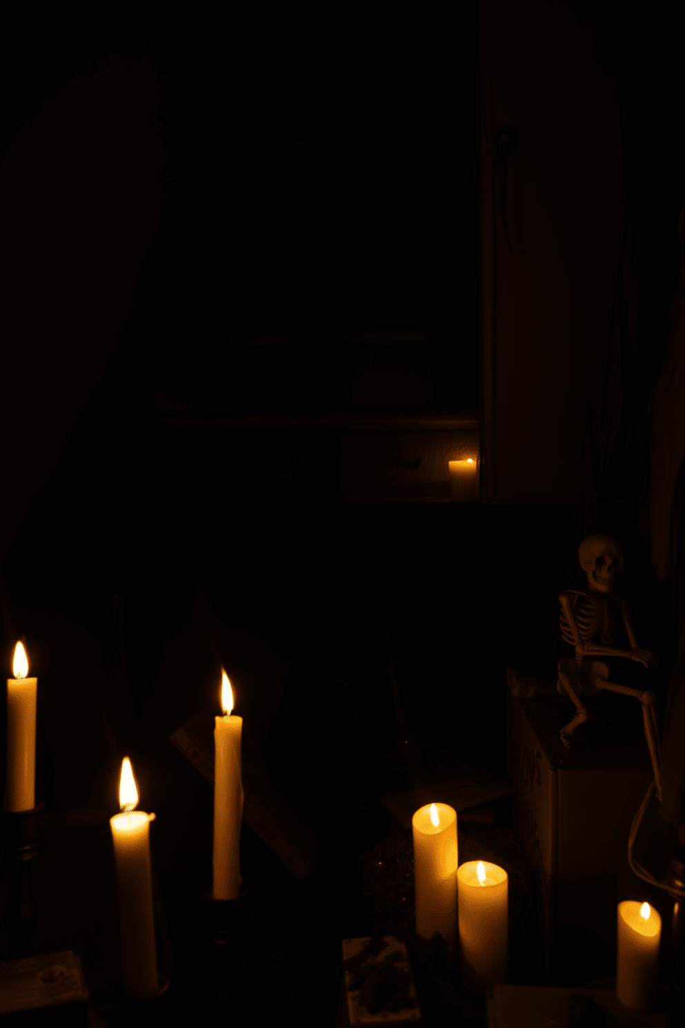 A dimly lit crawl space under the stairs creates an eerie atmosphere perfect for Halloween. Shadows dance across the walls, and cobwebs hang from the ceiling, adding to the unsettling vibe. Scattered around the space are old, dusty boxes and forgotten items, enhancing the feeling of abandonment. Flickering LED candles cast an ominous glow, while spooky decorations like skeletons and bats complete the chilling decor.