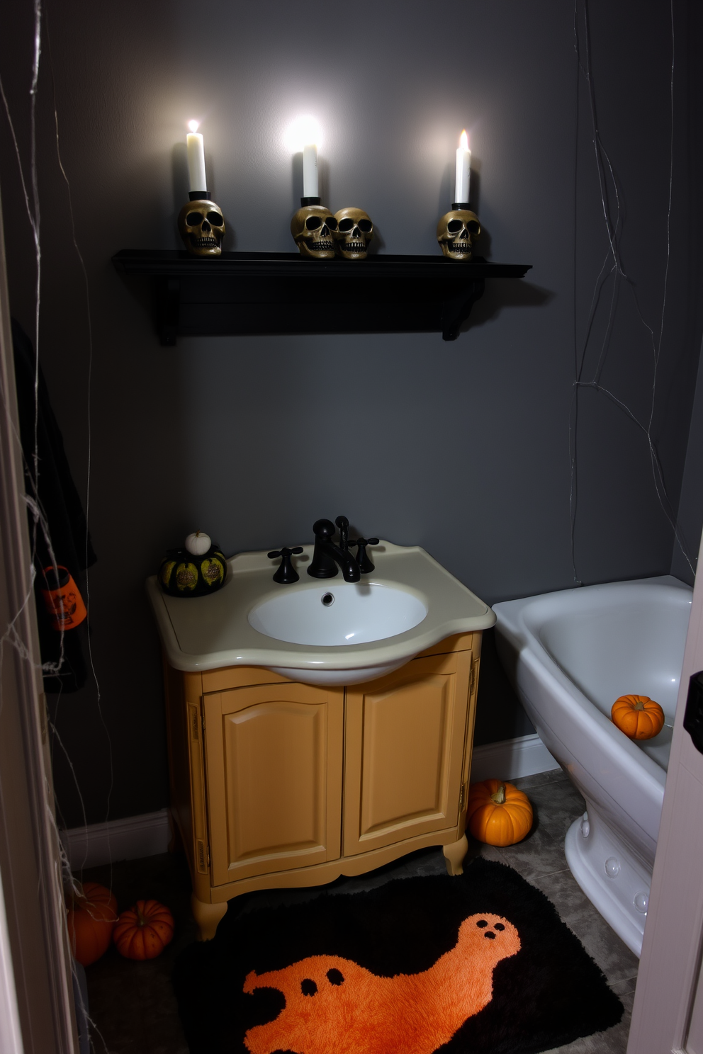 A spooky Halloween bathroom setting featuring creepy candle holders shaped like skulls. The candle holders are placed on a dark wooden shelf above a vintage sink, casting eerie shadows on the muted gray walls. A black and orange color scheme dominates the decor, with a plush bath mat displaying a ghostly design. Cobwebs are draped in the corners, and a few small pumpkins are scattered around to enhance the Halloween theme.