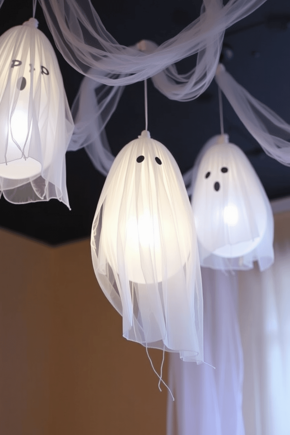 DIY floating ghosts hanging from ceiling. The ghosts are made from white cheesecloth draped over balloons, giving them an ethereal look. Soft LED lights illuminate the ghosts from below, creating a spooky glow. Wispy strands of tulle hang from the ceiling to enhance the ghostly effect.