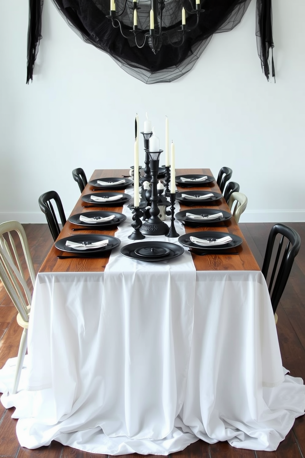 A ghostly white tablecloth drapes elegantly over a long wooden dining table, adorned with black accent pieces such as candles and decorative plates. Surrounding the table are mismatched chairs in dark tones, creating a cozy yet eerie atmosphere perfect for Halloween gatherings.