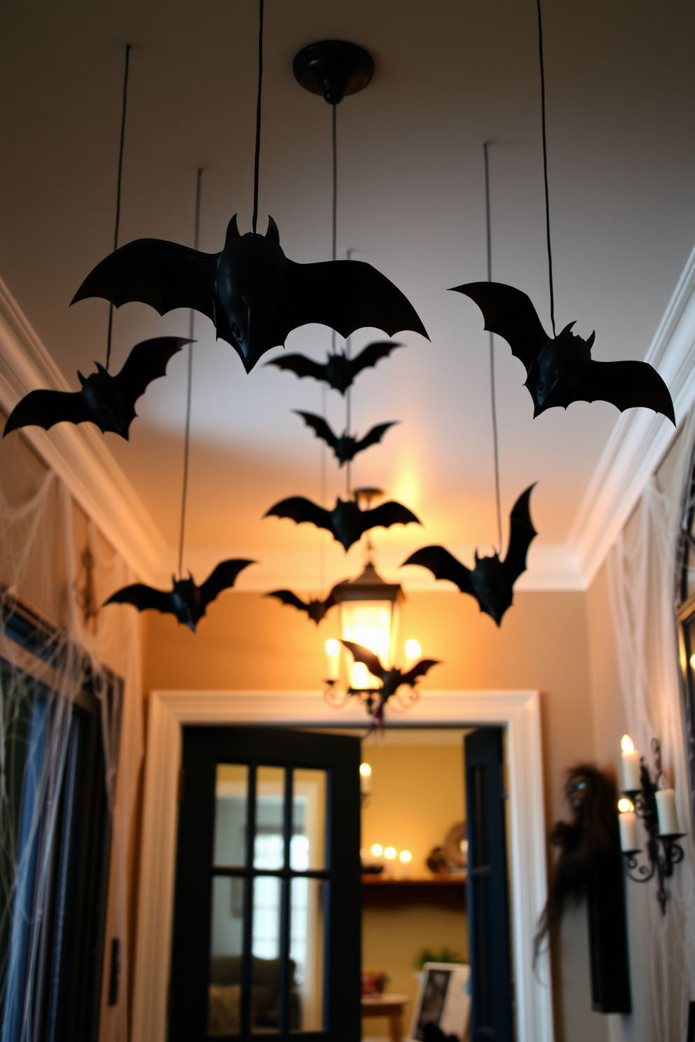 A whimsical Halloween entryway features hanging bats suspended from the ceiling, creating a spooky atmosphere for guests. The walls are adorned with cobwebs and flickering candlelight, enhancing the festive spirit of the season.