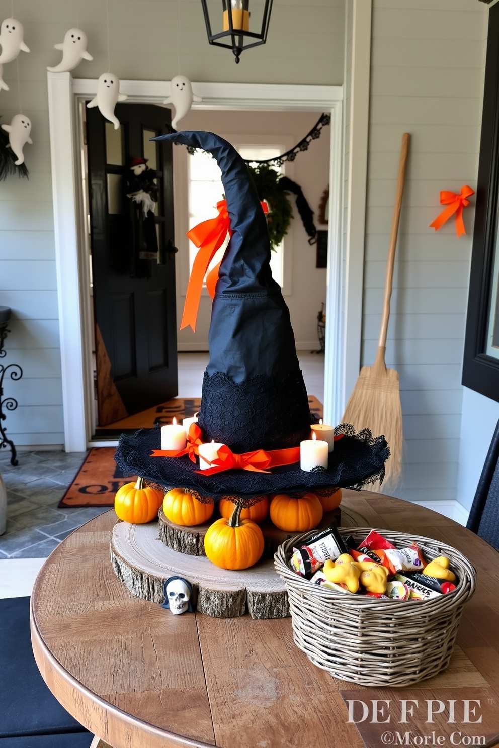 A whimsical witch hat centerpiece sits atop a rustic wooden table, surrounded by small pumpkins and flickering candles. The hat is adorned with black lace and vibrant orange ribbons, creating a playful yet elegant focal point for the Halloween decor. The entryway is transformed into a spooky haven with hanging ghost decorations and a welcome mat featuring a festive design. A broom leans against the wall, and a basket filled with assorted Halloween treats invites guests to indulge in the seasonal spirit.