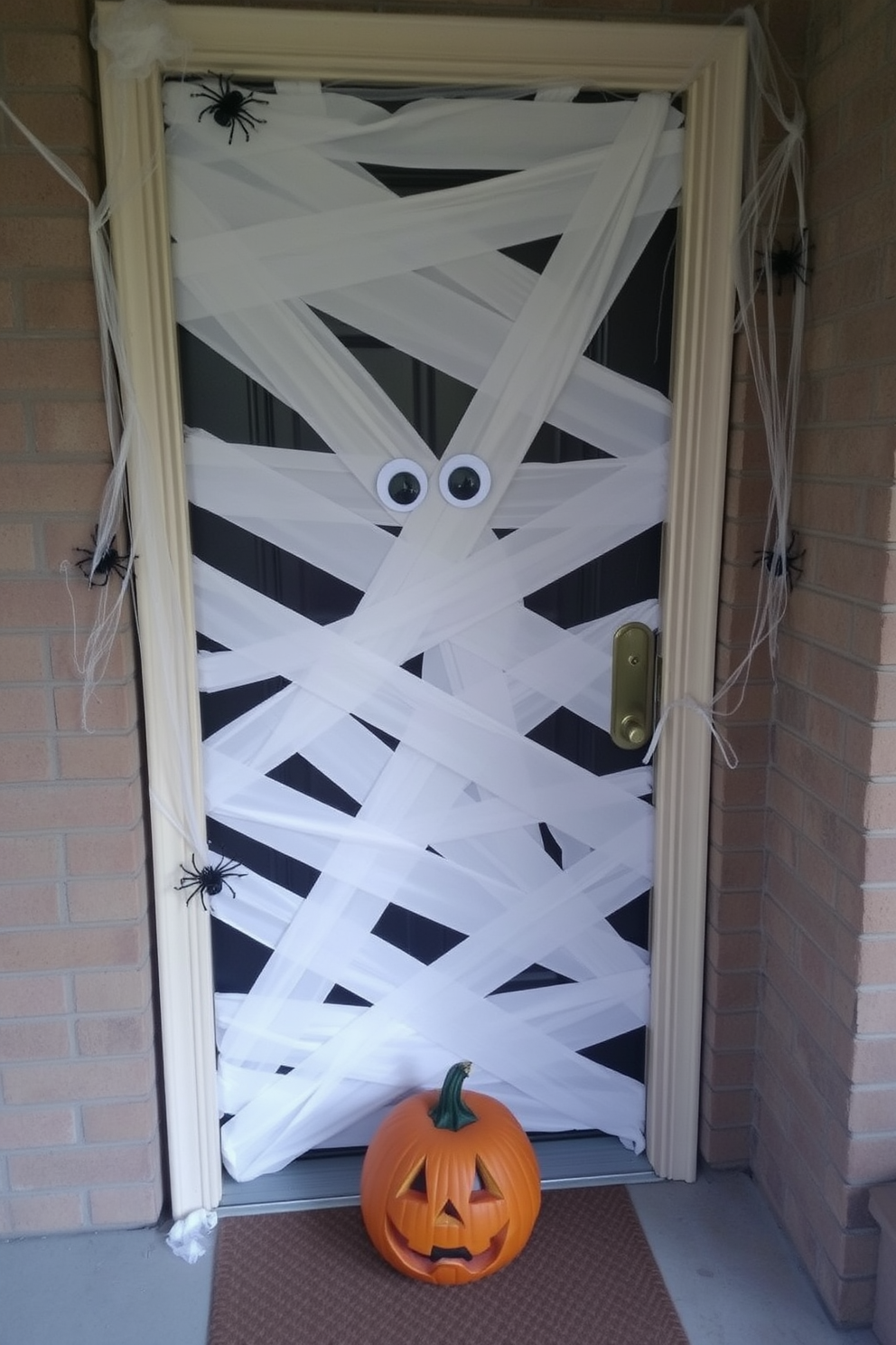 A mummy-wrapped door creates a spooky and festive atmosphere for Halloween. The door is covered in strips of white fabric, resembling bandages, with googly eyes placed at the center for an added touch of fright. To enhance the eerie effect, add fake cobwebs and plastic spiders around the doorframe. A pumpkin with a carved face sits at the base, completing the Halloween theme and inviting trick-or-treaters.