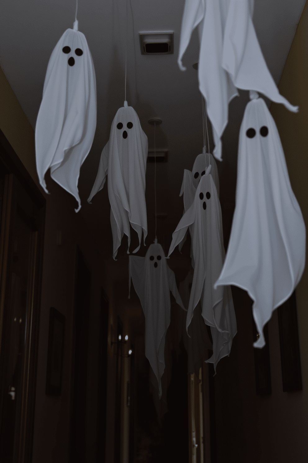 A spooky Halloween hallway adorned with hanging ghost decorations. The ghosts are made of white fabric, gently swaying from the ceiling, creating an eerie atmosphere.