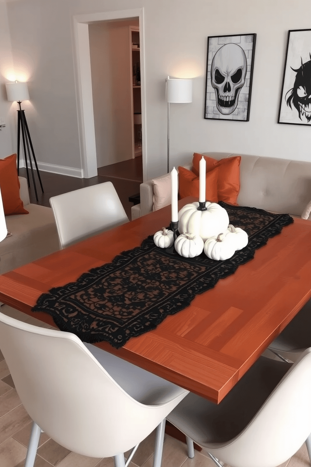 A chic black lace table runner drapes elegantly over a polished wooden dining table. Surrounding the table are modern chairs with sleek lines, and the centerpiece features a collection of white pumpkins and candles for a festive touch. The living room is adorned with plush velvet cushions in deep orange and gold hues, creating a cozy atmosphere. Soft lighting from stylish floor lamps enhances the ambiance, while a spooky artwork piece hangs on the wall, adding a playful Halloween element.