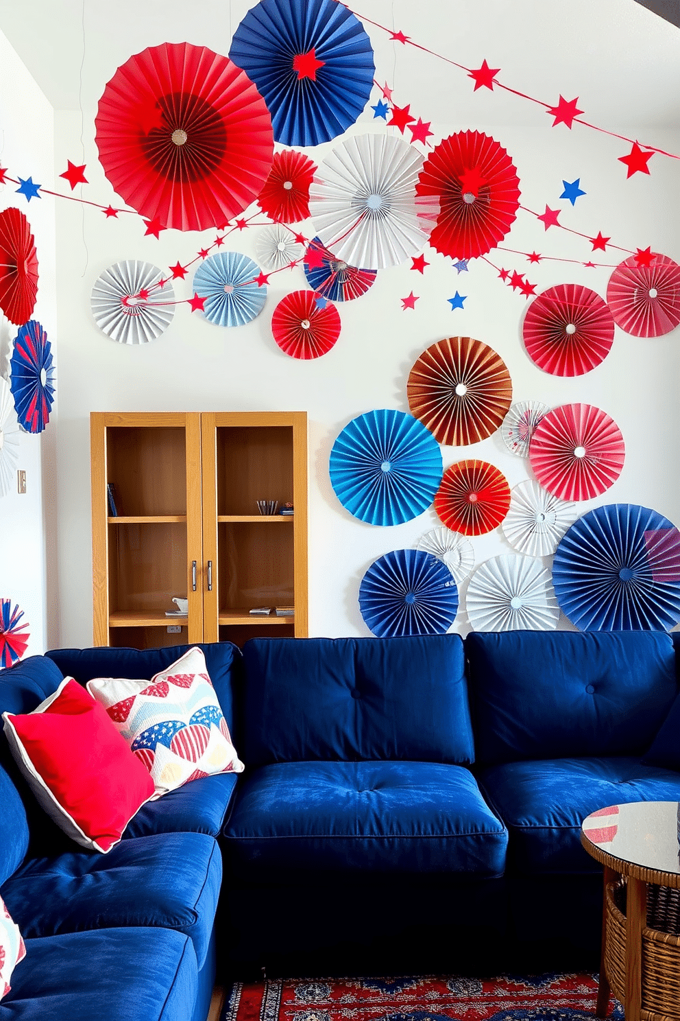 A vibrant living room adorned with decorative fans in red, white, and blue. The walls are painted in a crisp white, creating a fresh backdrop for the festive accents. In the center, a plush navy sofa is complemented by bright red and white throw pillows. An arrangement of star-spangled decorations hangs from the ceiling, adding a playful touch to the Independence Day theme.