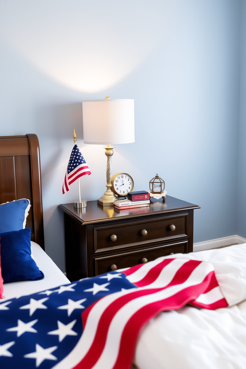 A stylish bedroom featuring a nightstand adorned with flag-themed accessories to celebrate Independence Day. The nightstand is topped with a small American flag, a decorative red white and blue lamp, and a vintage clock that adds a touch of nostalgia. The walls are painted in a soft blue hue, creating a serene backdrop for the festive decor. A patriotic throw blanket is draped over the edge of the bed, complementing the overall theme and enhancing the cozy atmosphere.