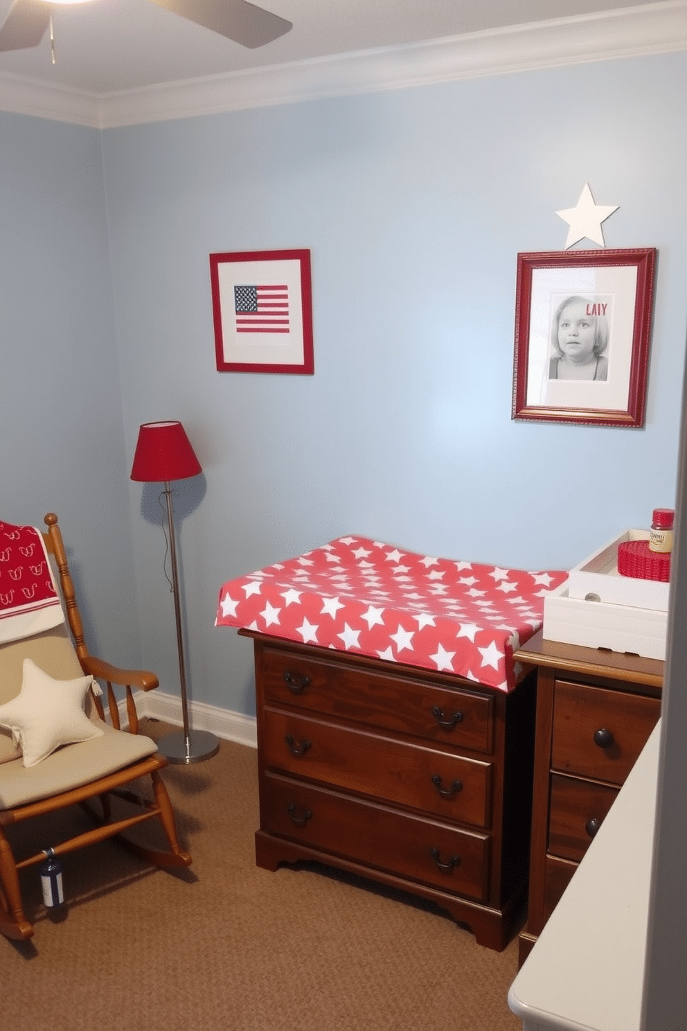 A charming nursery featuring a star and stripe patterned changing pad cover. The walls are painted in a soft blue hue, complemented by red and white accents throughout the room. A cozy rocking chair sits in the corner, adorned with a plush throw pillow that matches the changing pad cover. A wooden dresser with a star motif provides storage for baby essentials, while framed patriotic artwork decorates the walls.