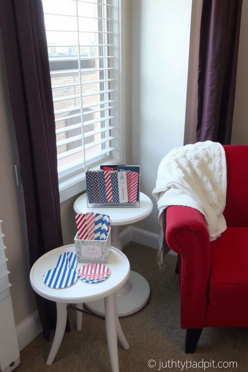 A cozy reading nook decorated for Independence Day. The space features a comfortable armchair upholstered in red fabric, paired with a small white side table adorned with blue and white striped coasters. Red, white, and blue themed bookmarks are displayed in a decorative holder on the table. A patriotic throw blanket drapes over the armchair, adding warmth and a festive touch to the nook.