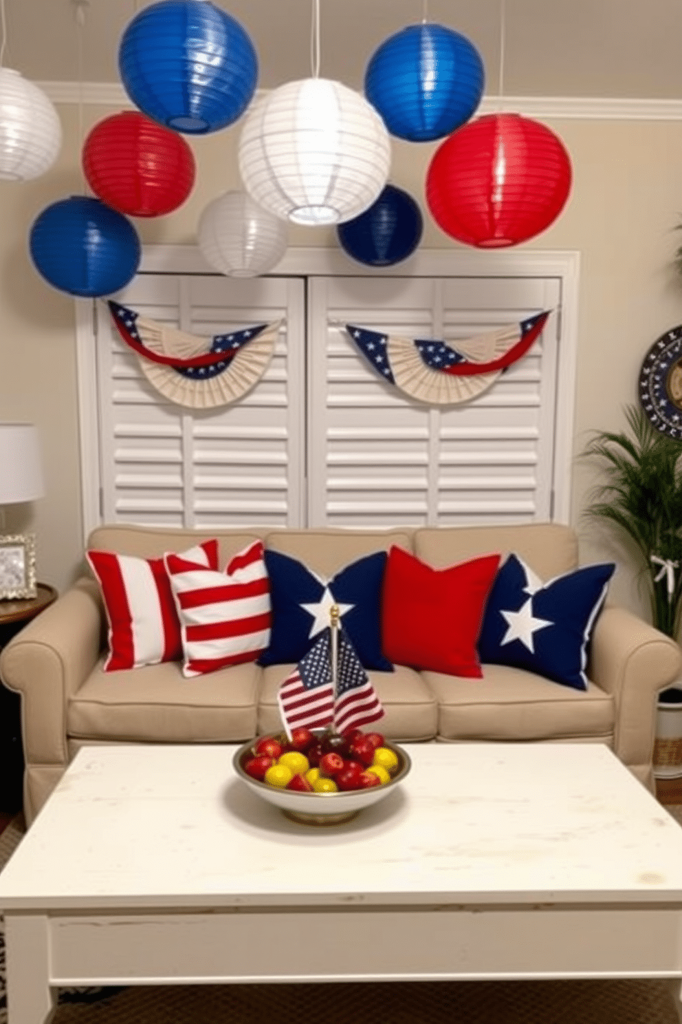 A cozy small living room decorated for Independence Day. The space features hanging paper lanterns in red, white, and blue, creating a festive atmosphere. A comfortable sofa is adorned with patriotic throw pillows in matching colors. A coffee table is set with a bowl of fresh fruit and a small American flag as a centerpiece.