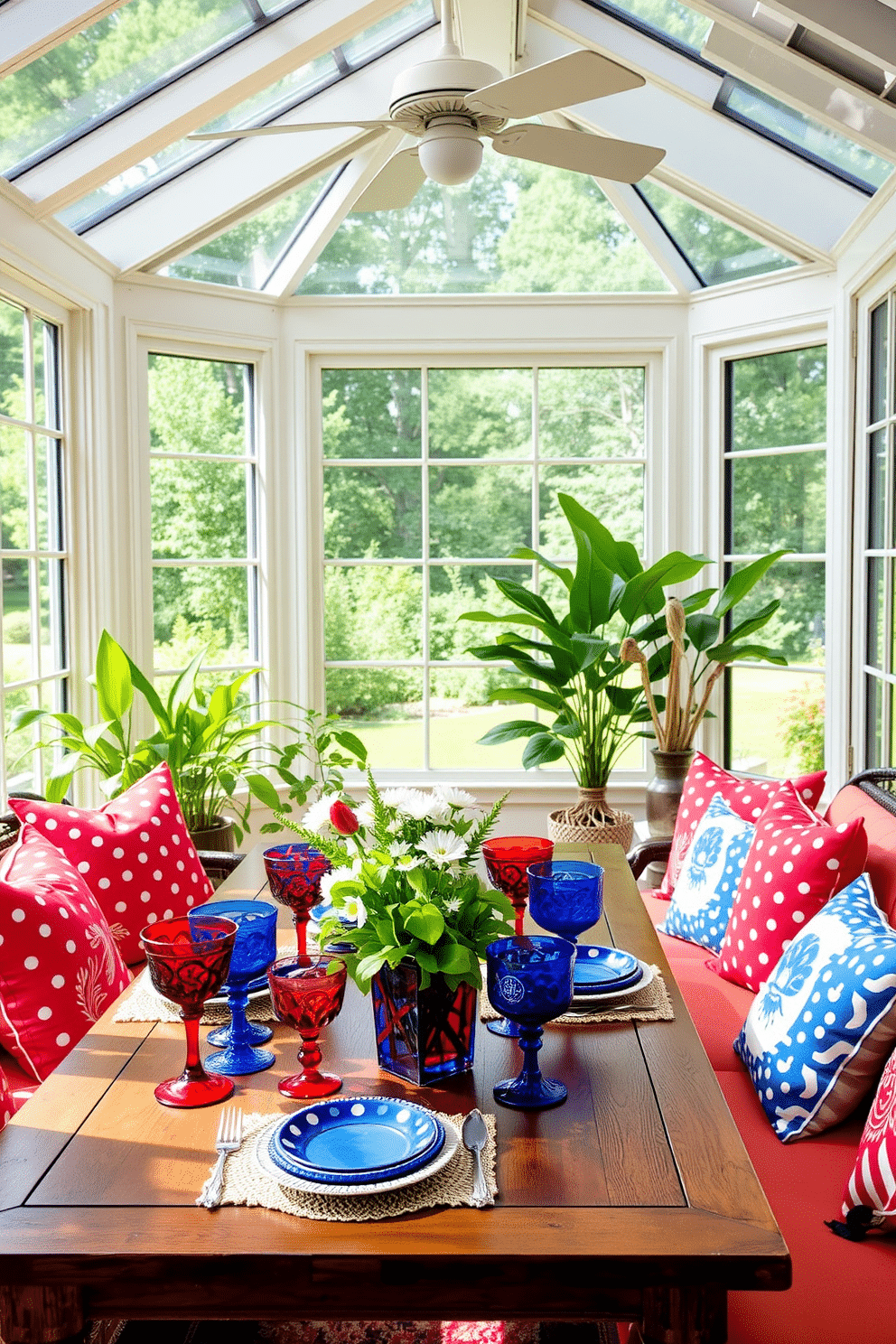 A vibrant sunroom filled with natural light. The decor features a mix of red and blue glassware elegantly arranged on a wooden table, celebrating Independence Day. Bright cushions in patriotic colors adorn the seating area, creating a festive atmosphere. Lush green plants are placed in the corners, enhancing the cheerful ambiance of the space.